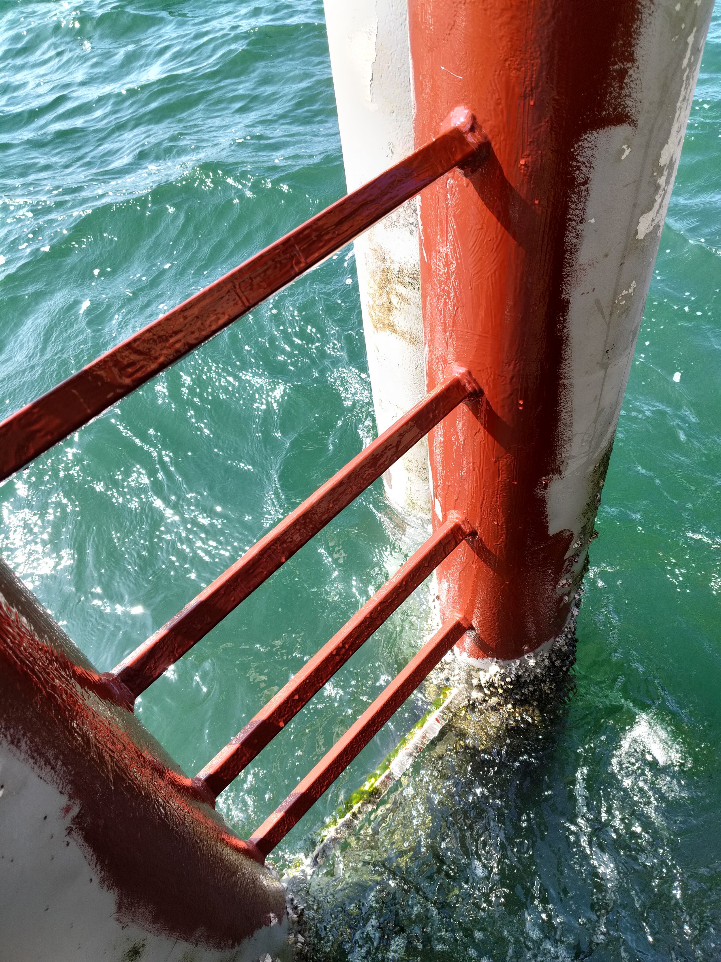 Close-up of a red and white boat railing against blue water.