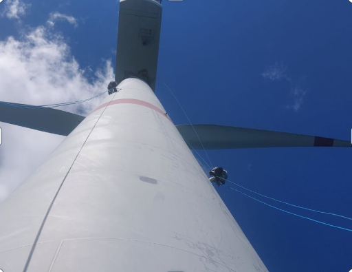 View from the base of a wind turbine looking up at the blades against a blue sky.