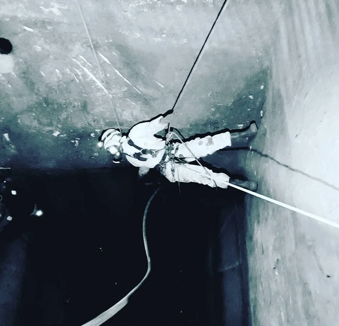 A person wearing rock climbing gear ascending a vertical cave wall at night.