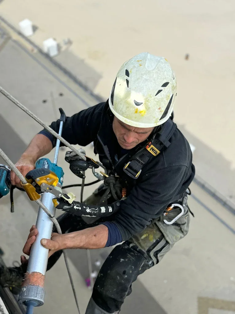 A construction worker wearing a safety helmet and harness working on a metal pipe at a construction site.