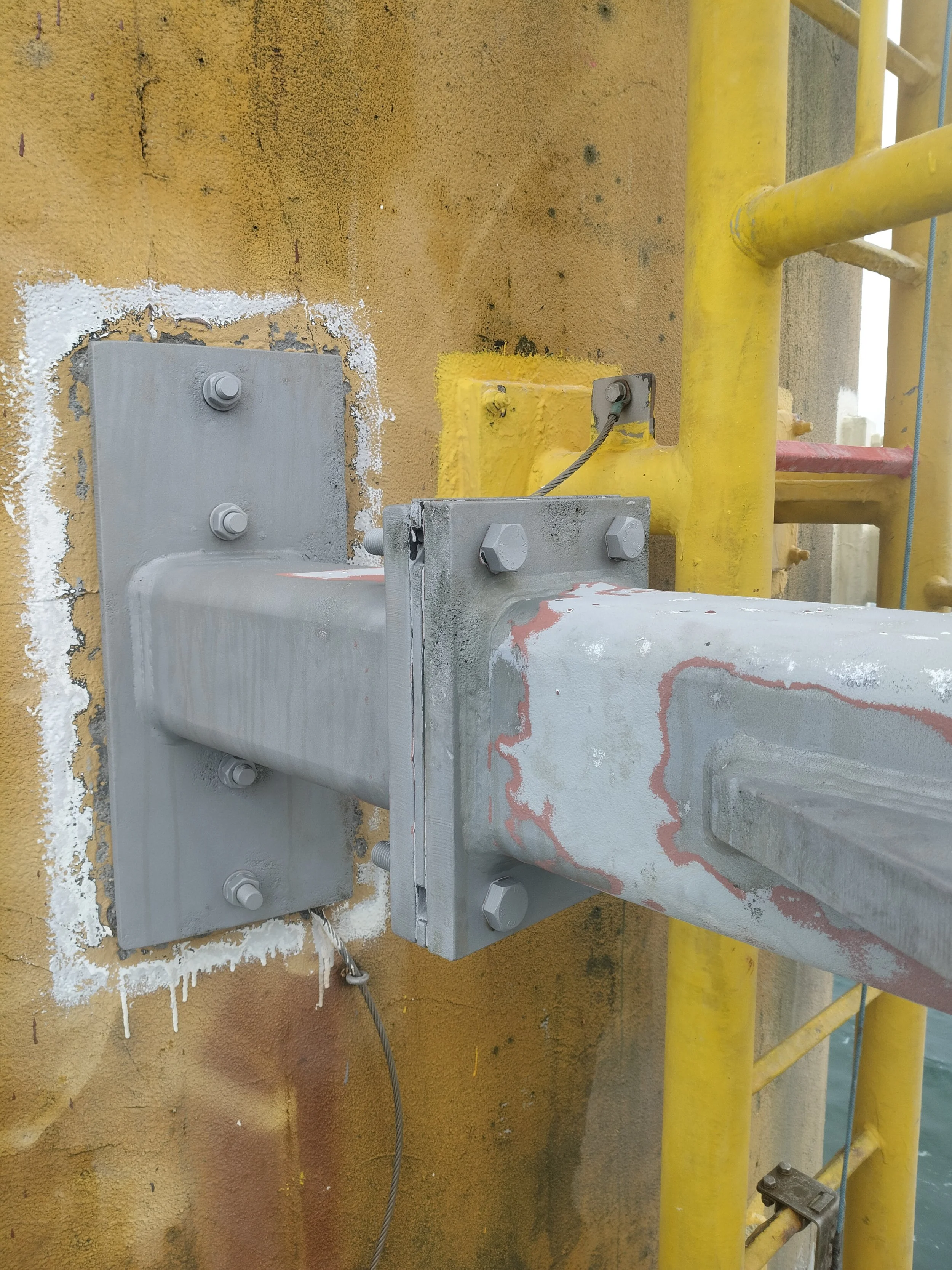 Close-up of a construction site showing a metal attachment on a concrete wall, with yellow scaffolding nearby.