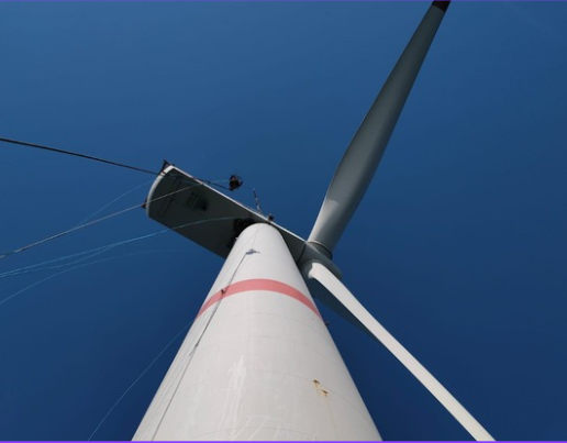 Looking up at a wind turbine against a clear blue sky.