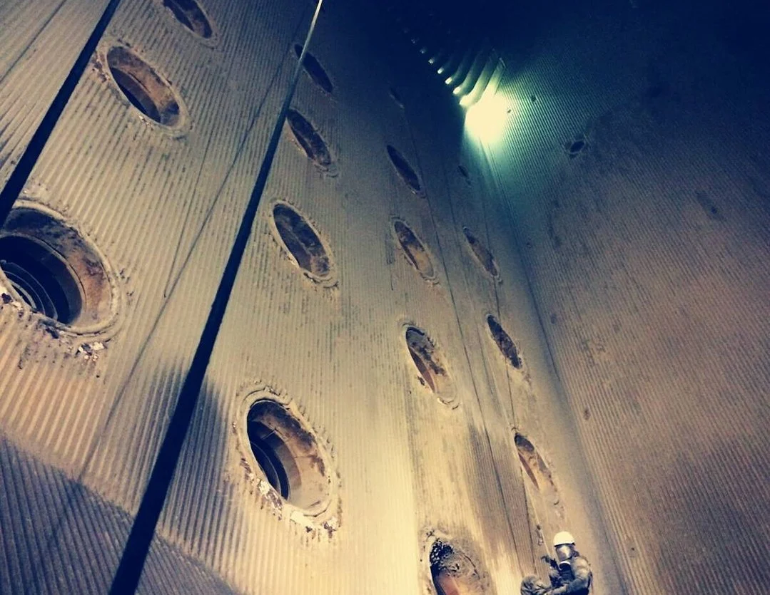 A construction worker wearing a hard hat working inside a large metallic industrial structure with multiple circular openings.