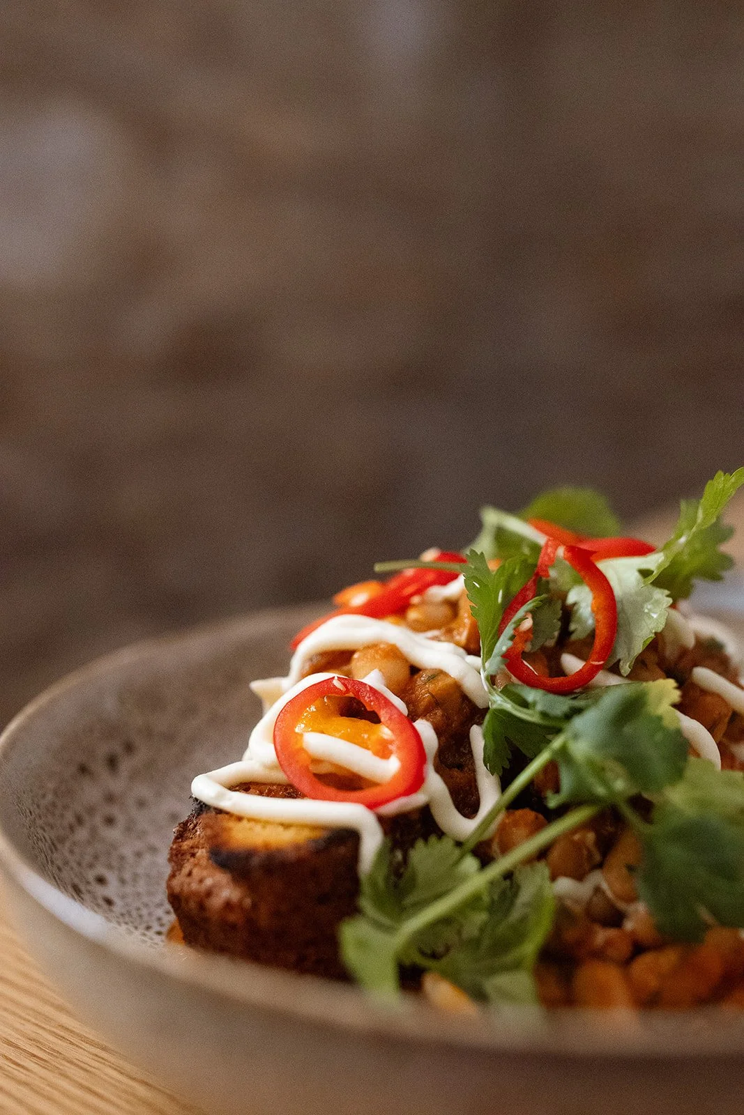 Close-up of a plated dish with grilled meat, garnished with sliced red chili peppers, fresh cilantro, green salad, and drizzled with white sauce, served on a white plate.