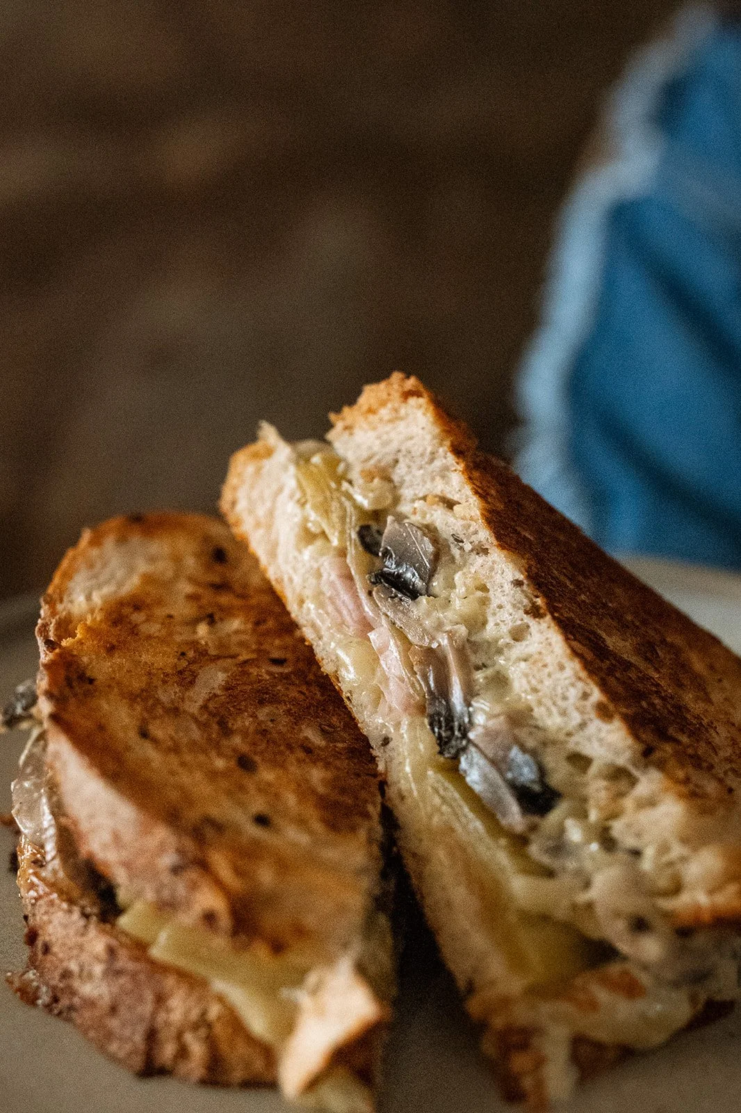 Close-up of a toasted sandwich cut in half, revealing melted cheese and mushrooms inside.