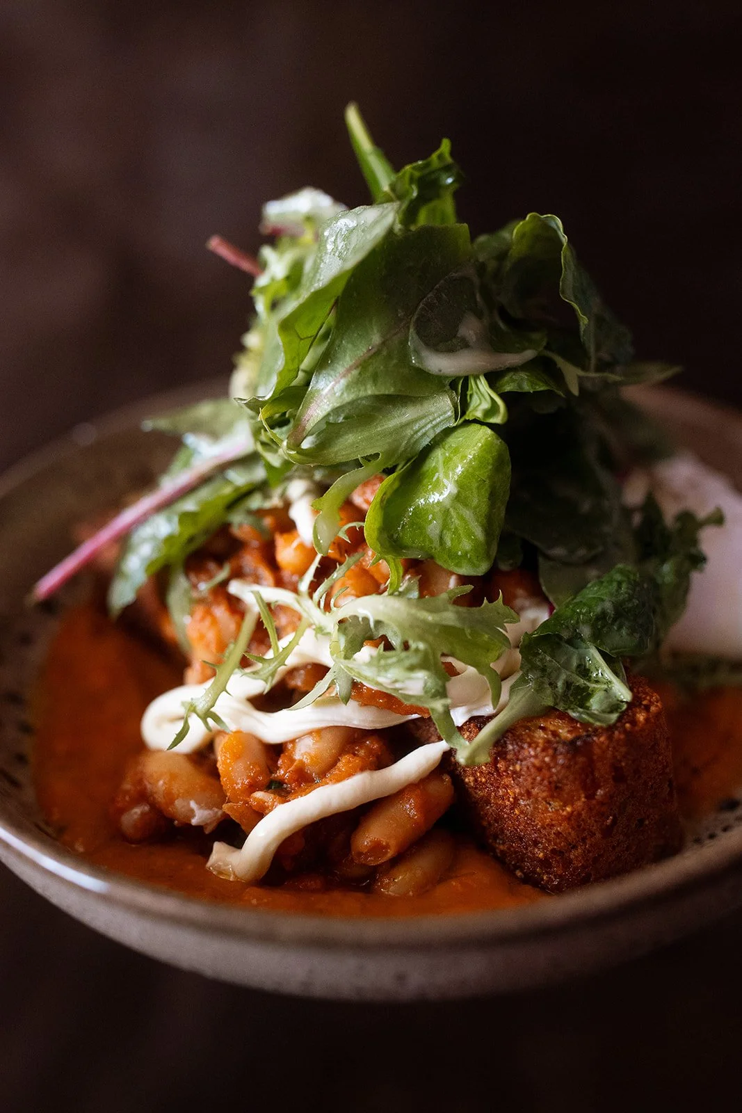 Close-up of a bowl of chili topped with fresh greens and sour cream.