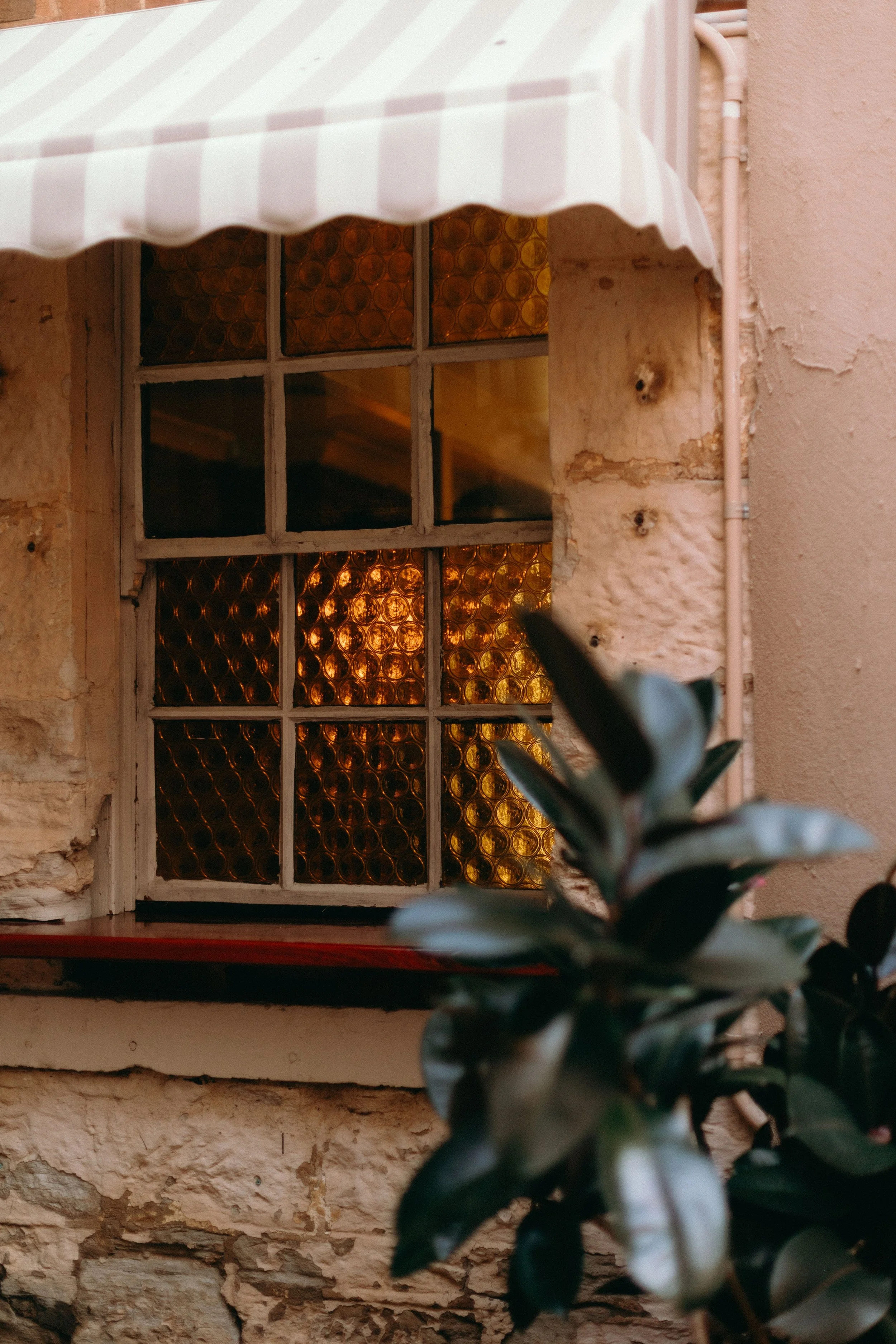 Image of takeaway window at Goldies Cafe in DUbbo. Beige and white awning is shown with rustic walls surrounding the window. Retro yellow glass art deco style is on the panels of the window. Double hung window.