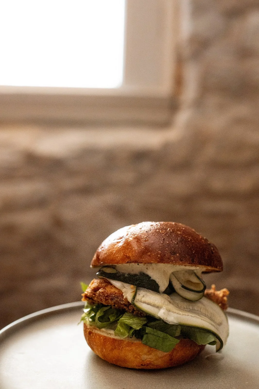 Image of fried chicken burger with cucumber sliced thinly and burger sauce on it