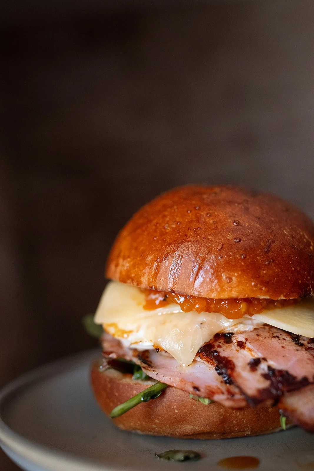 Close-up of a gourmet sandwich with grilled chicken, cheese, spinach, and sauce in a toasted bun.