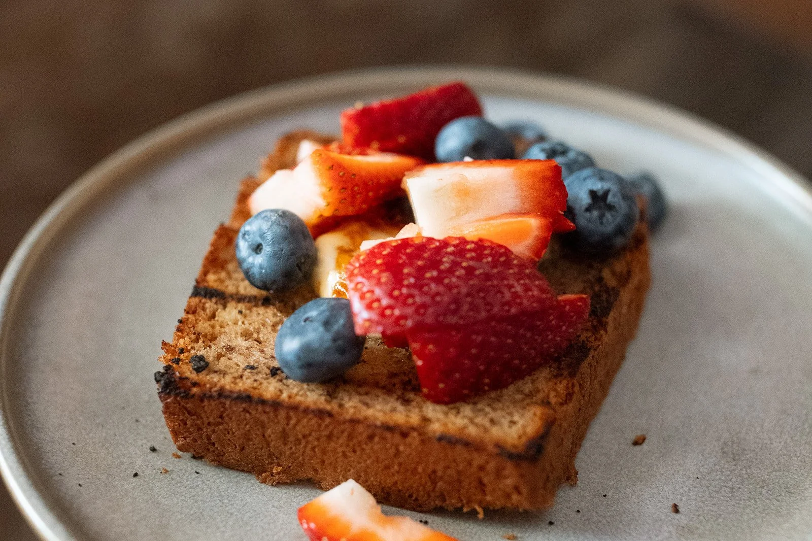 Slice of toast topped with fresh strawberries and blueberries.