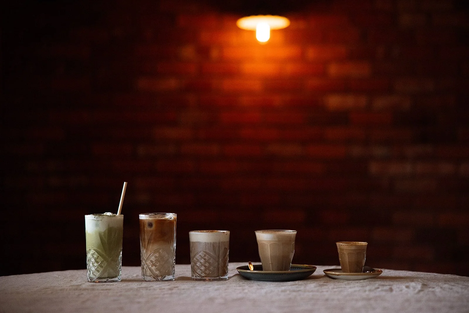 Five drinks of different sizes and types arranged on a table in front of a dimly lit brick wall.