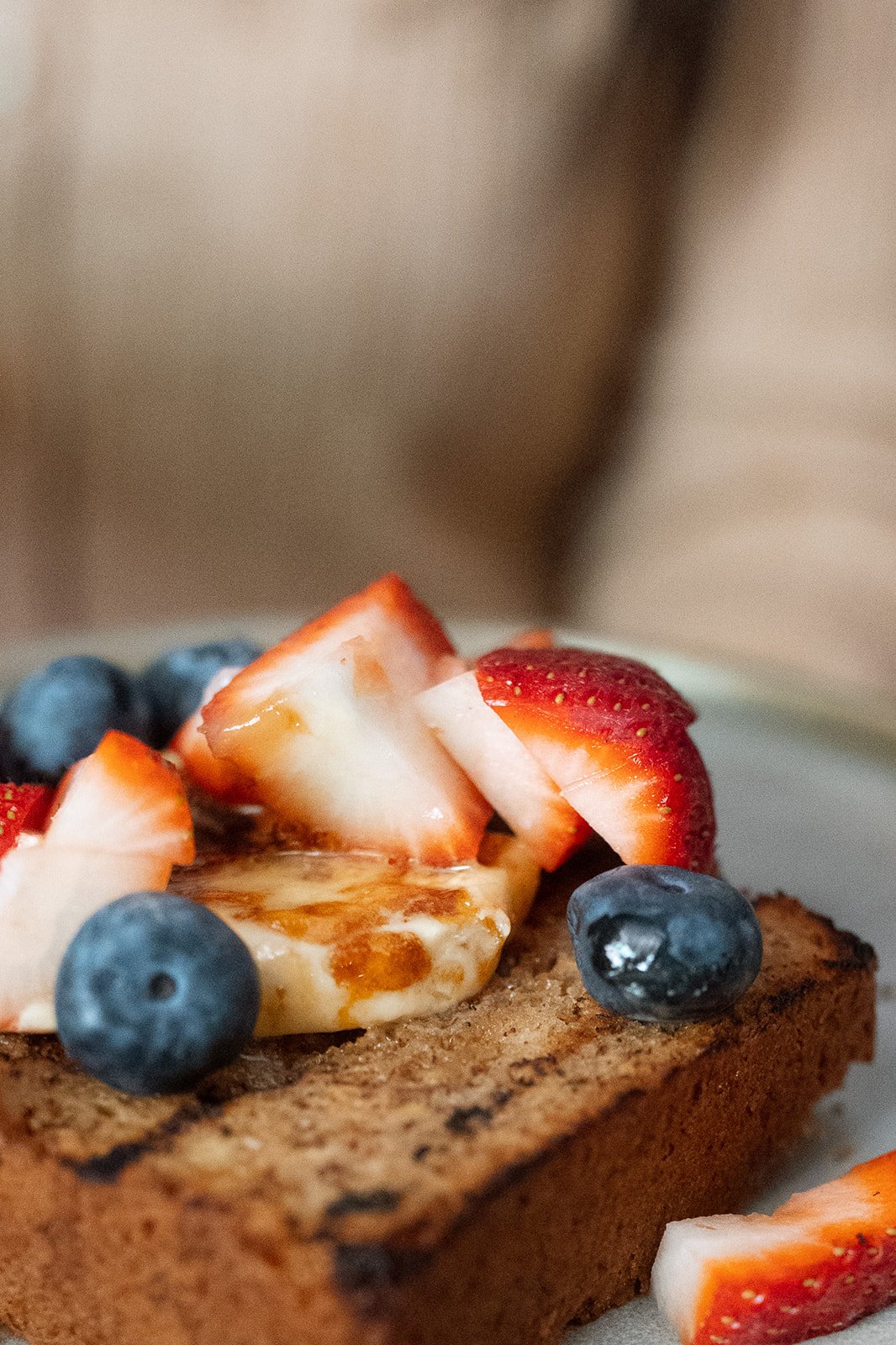 Close-up of a piece of toast topped with sliced strawberries, blueberries, and a dollop of cream or yogurt.