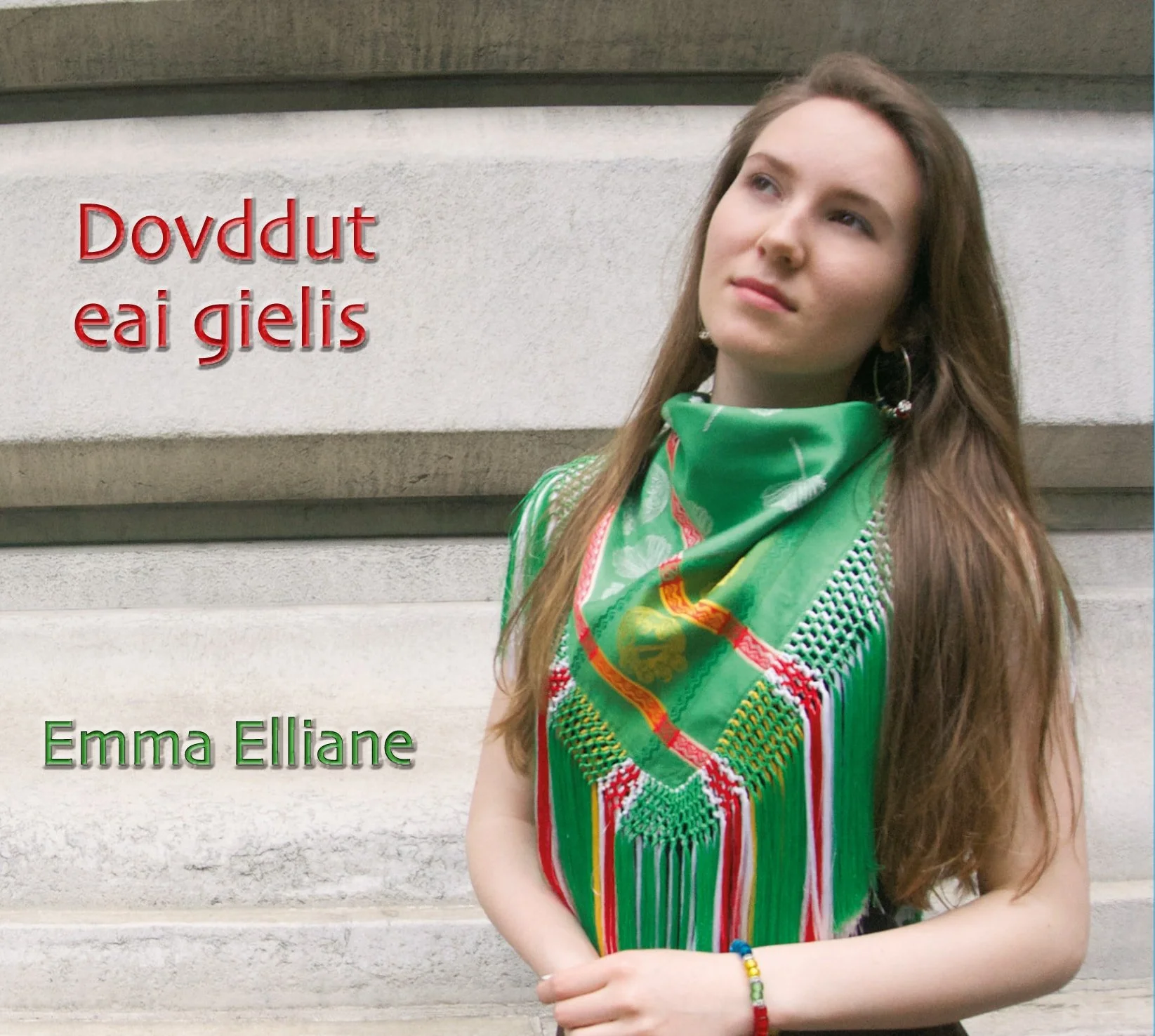 Cover of a book with a young woman with long brown hair wearing a green and red patterned scarf and earrings, standing against a stone wall, with the title 'Dovddut eai gielis' in red and author 'Emma Elliane' in green.