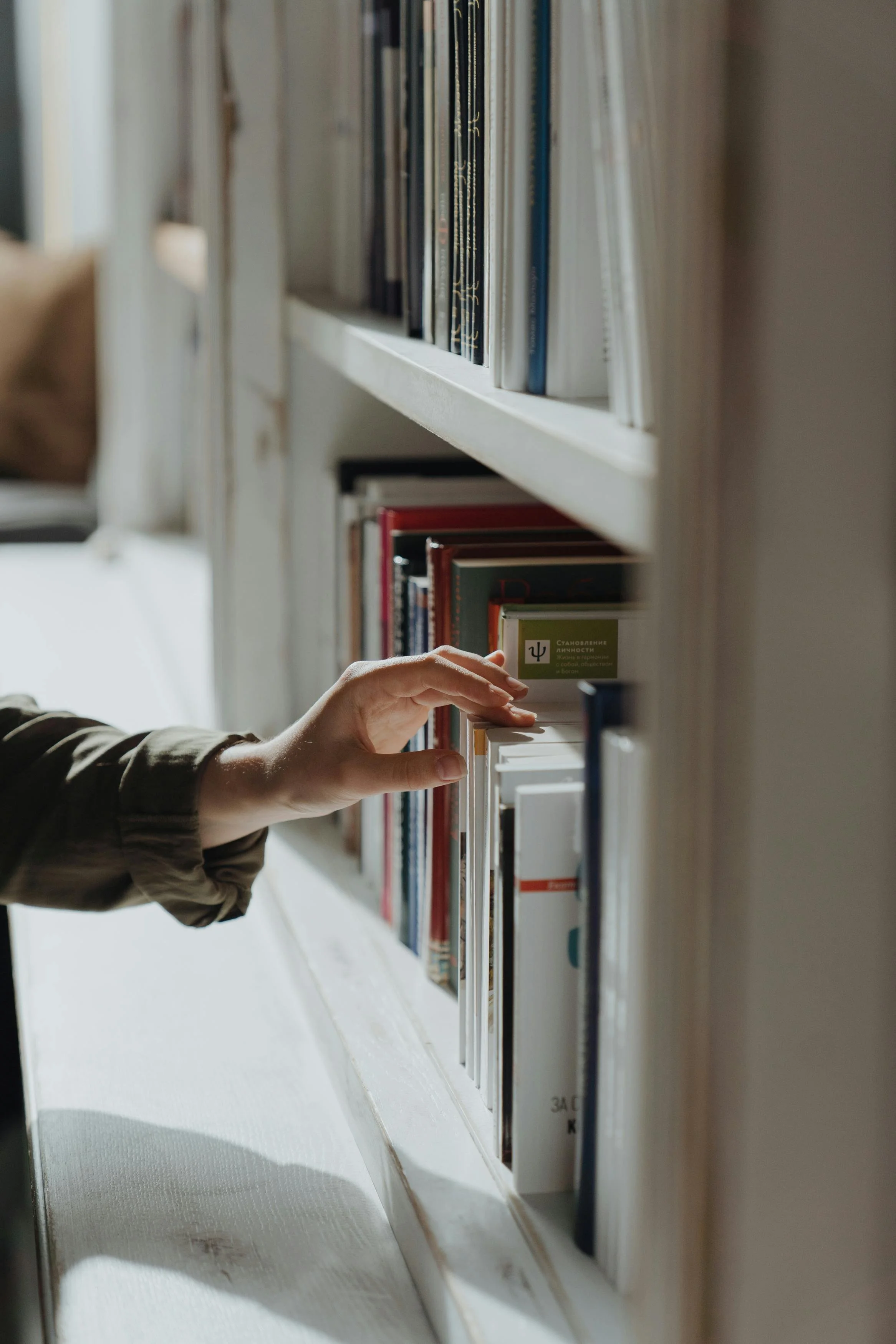 A person reaching for a book on a white bookshelf in a library or bookstore.