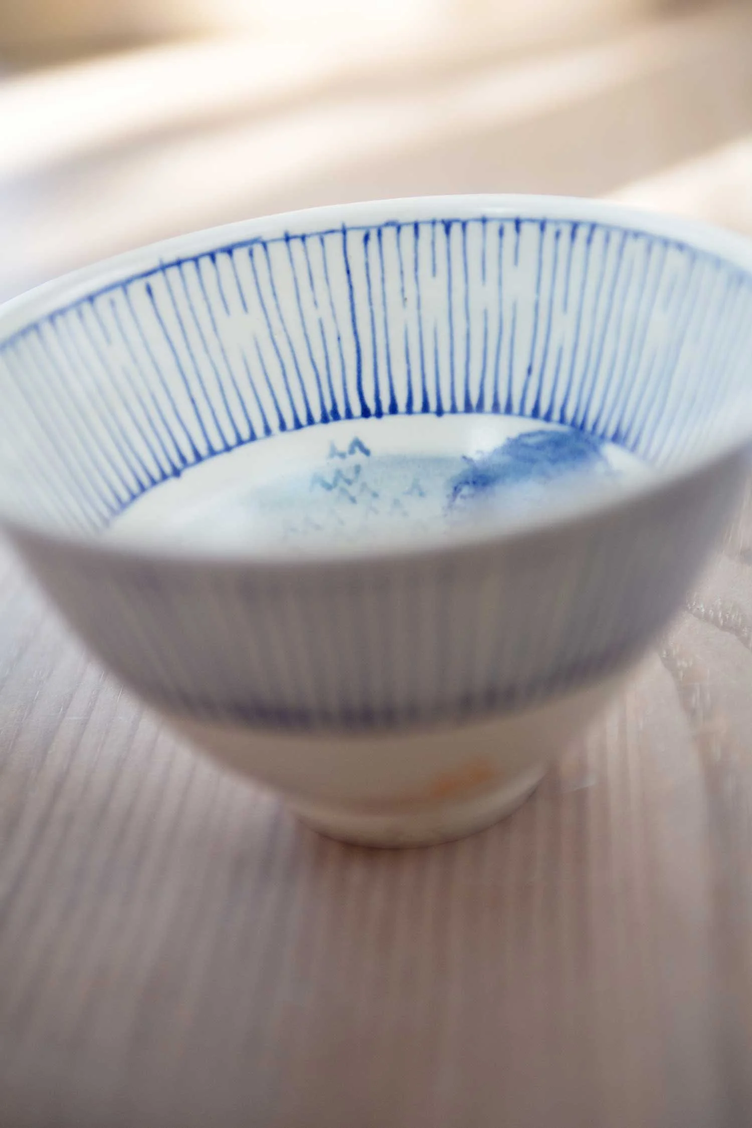A white stoneware bowl with blue vertical lines on the inside rim, seen from above.