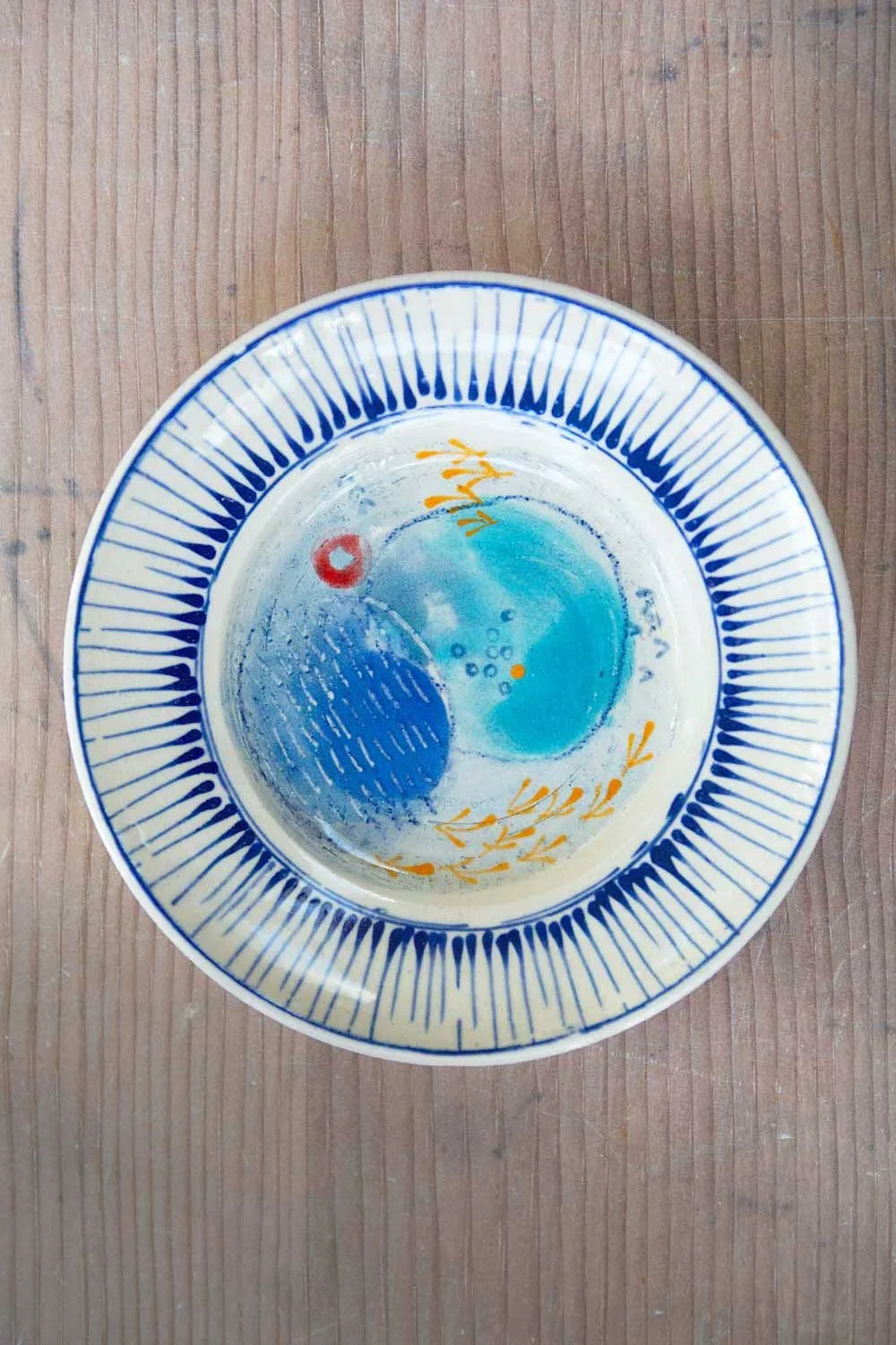 A handcrafted ceramic plate decorated with colourful patterns, placed on a wooden surface.