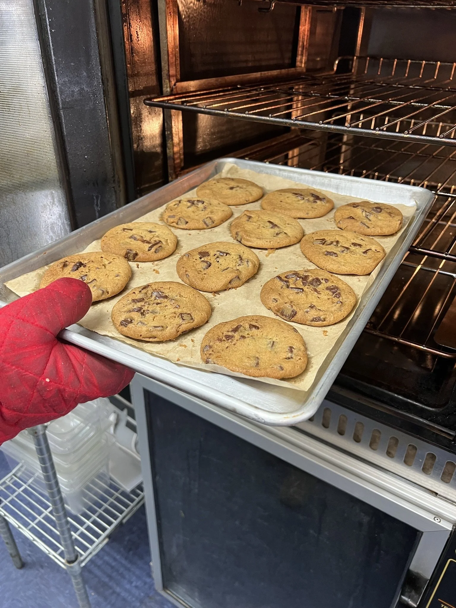 Elm Creek Beef A person in a red glove is holding a baking tray with chocolate chip cookies inside an oven.