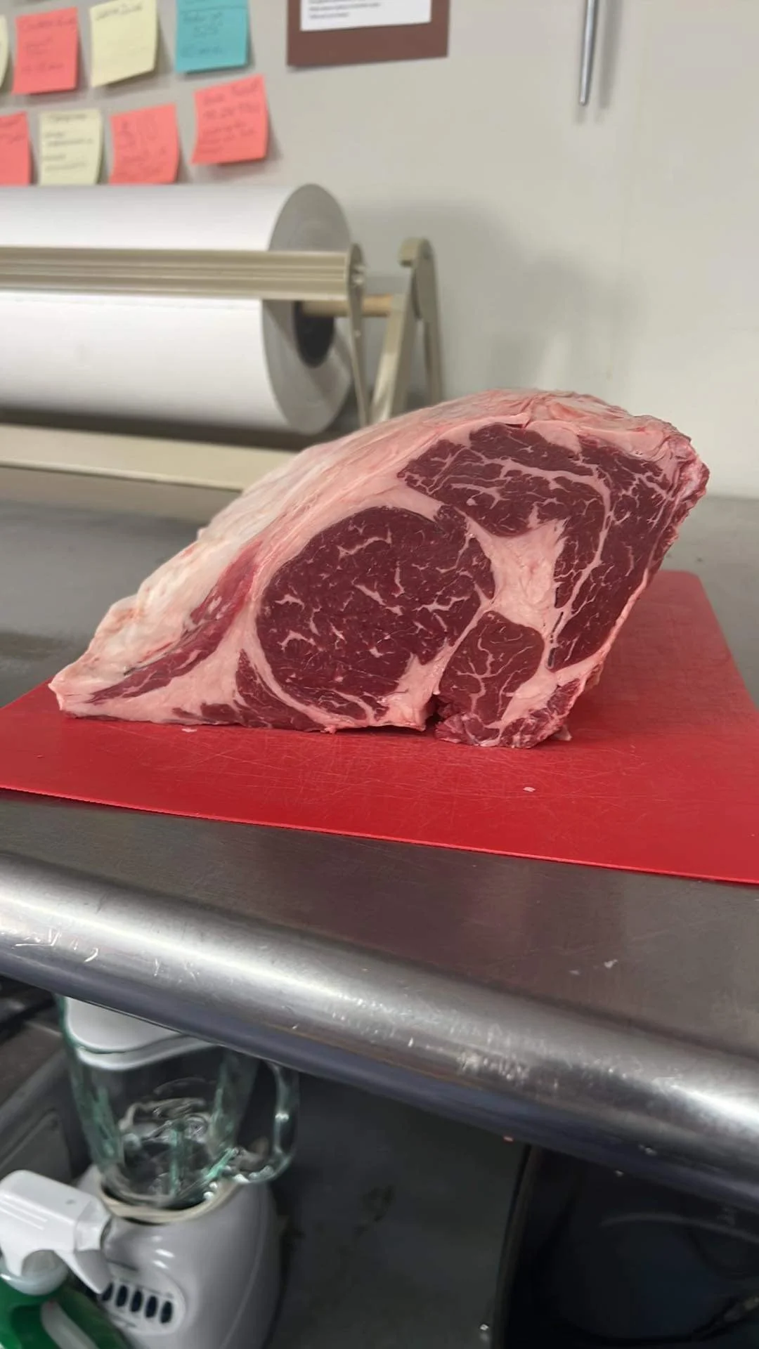 Elm Creek Beef A large cut of marbled raw beef on a red cutting board in a butcher shop or kitchen.