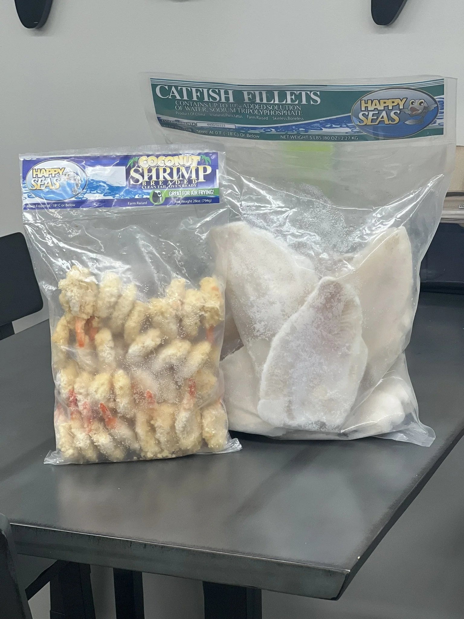 Elm Creek Beef Two large bags of frozen seafood on a gray table, one labeled 'Catfish Fillets' and the other labeled 'Coconut Shrimp'.