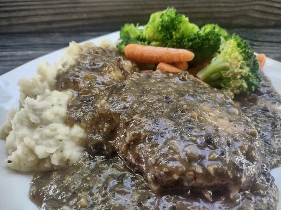 Elm Creek Beef Plate of mashed potatoes, a beef patty with gravy, steamed broccoli, and baby carrots.