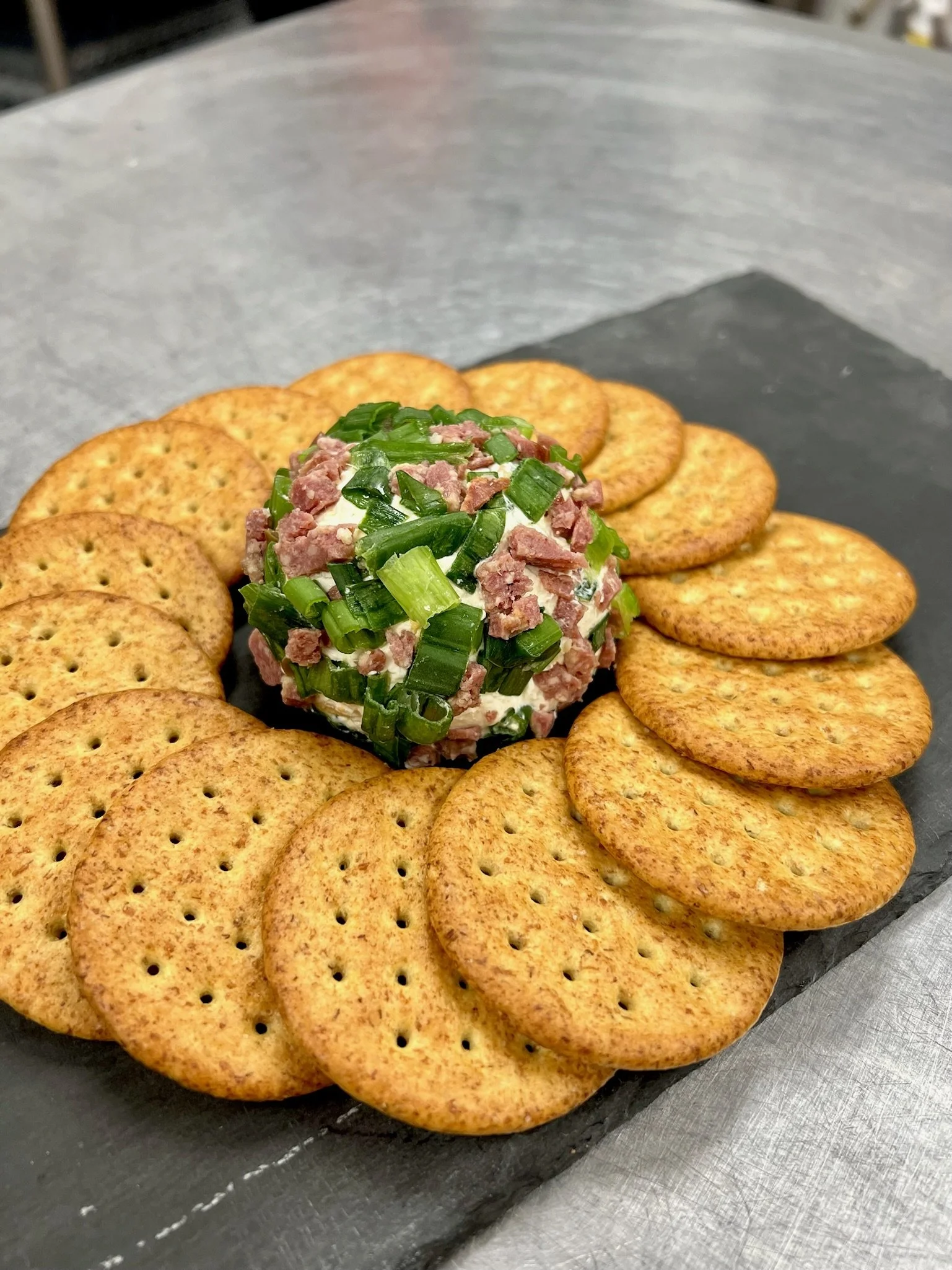 Elm Creek Beef A round arrangement of saltine crackers with a dollop of creamy spread topped with chopped green onions in the center.