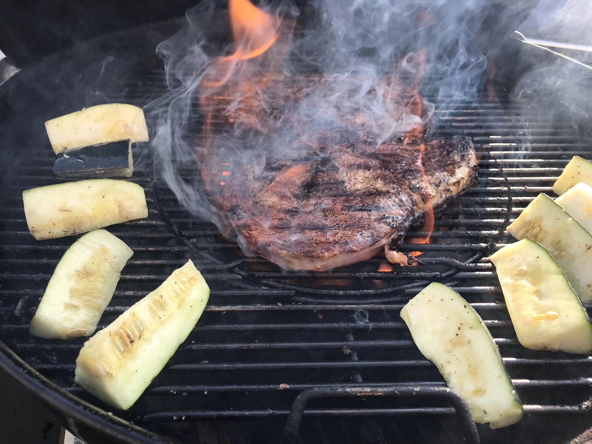 Elm Creek Beef Steak grilling on barbecue with slices of zucchini around it, smoke rising.