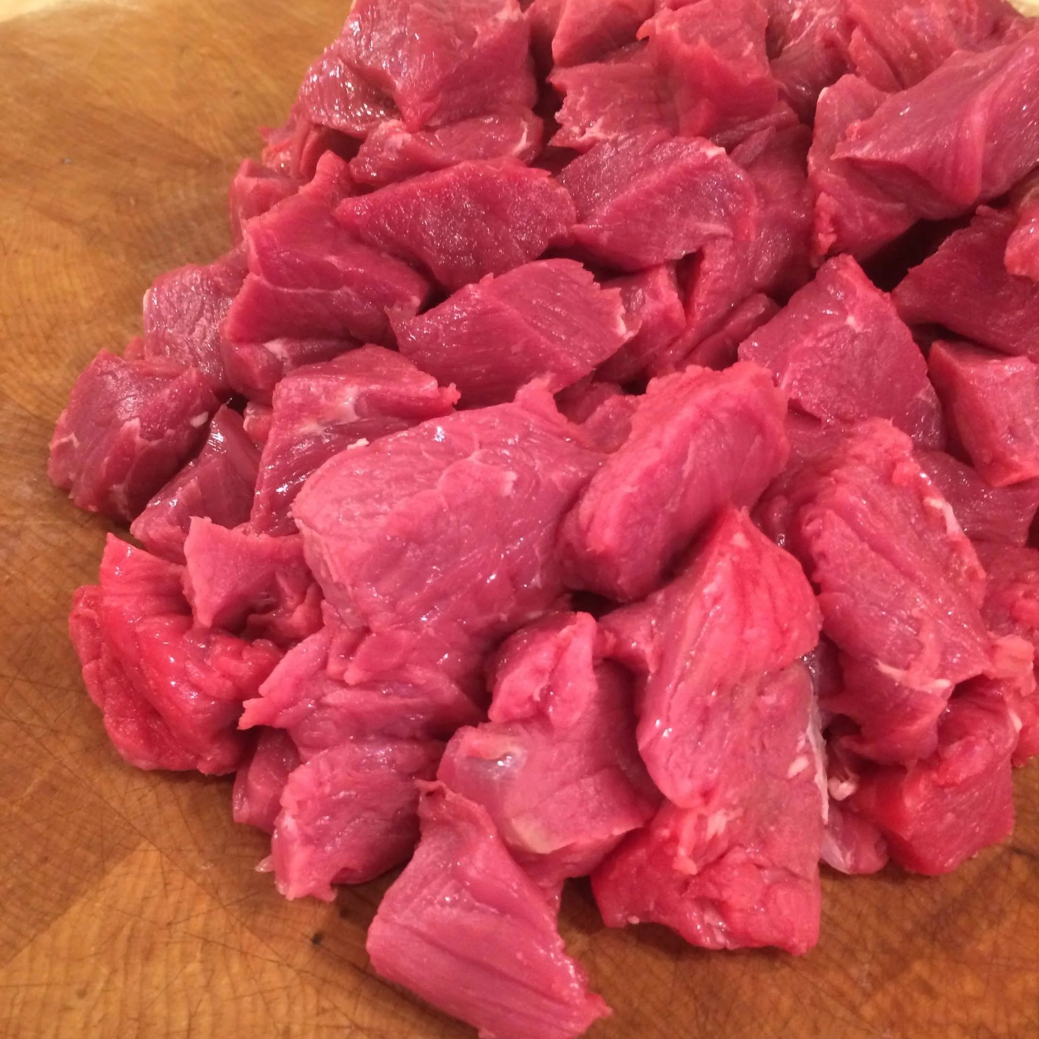 Elm Creek Beef Cubed raw beef on a wooden cutting board.