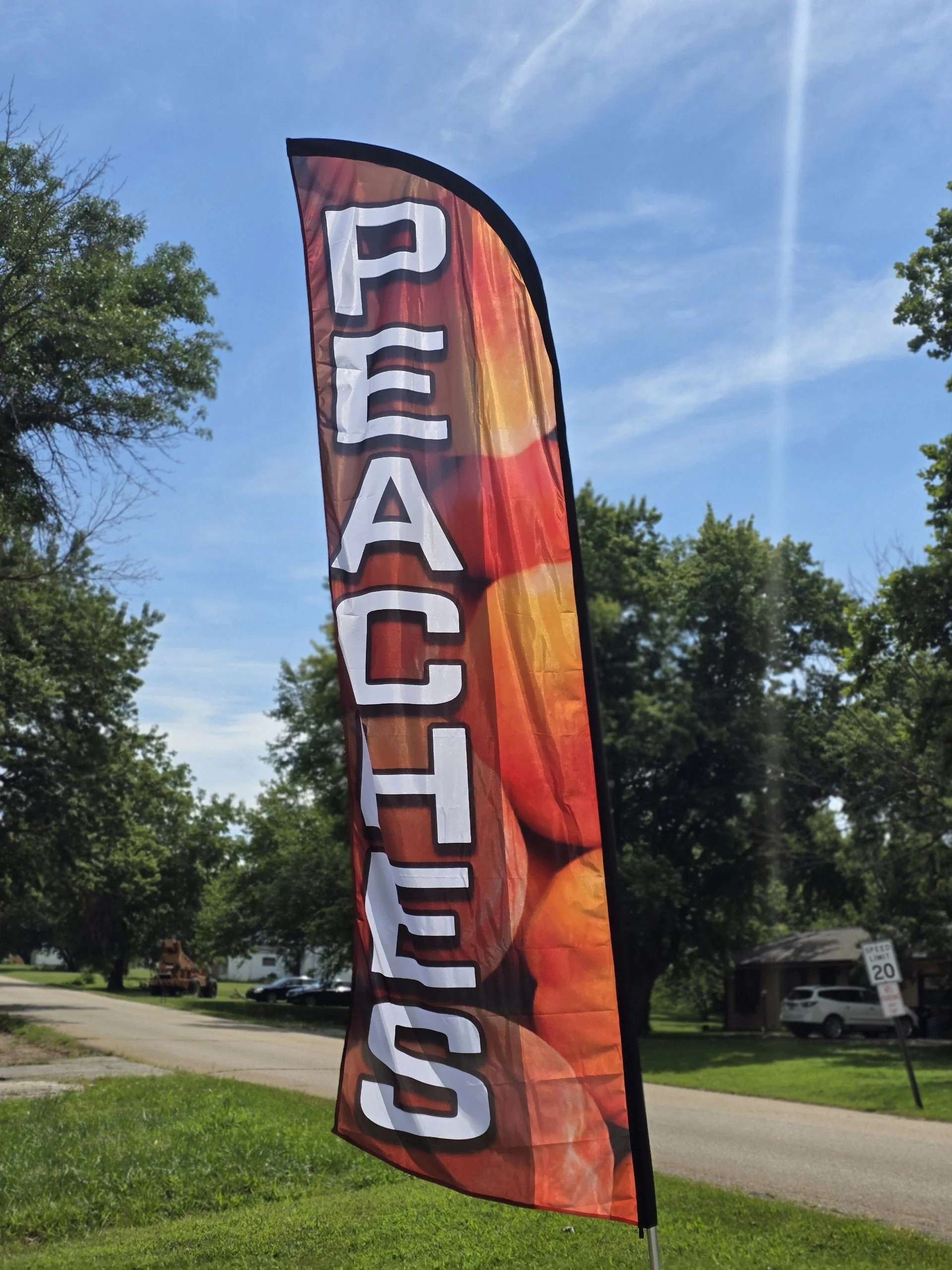 Elm Creek Beef A vertical flag with the words 'PEACH' in large white letters on a red, orange, and yellow background, set outdoors under a blue sky with some trees in the background.