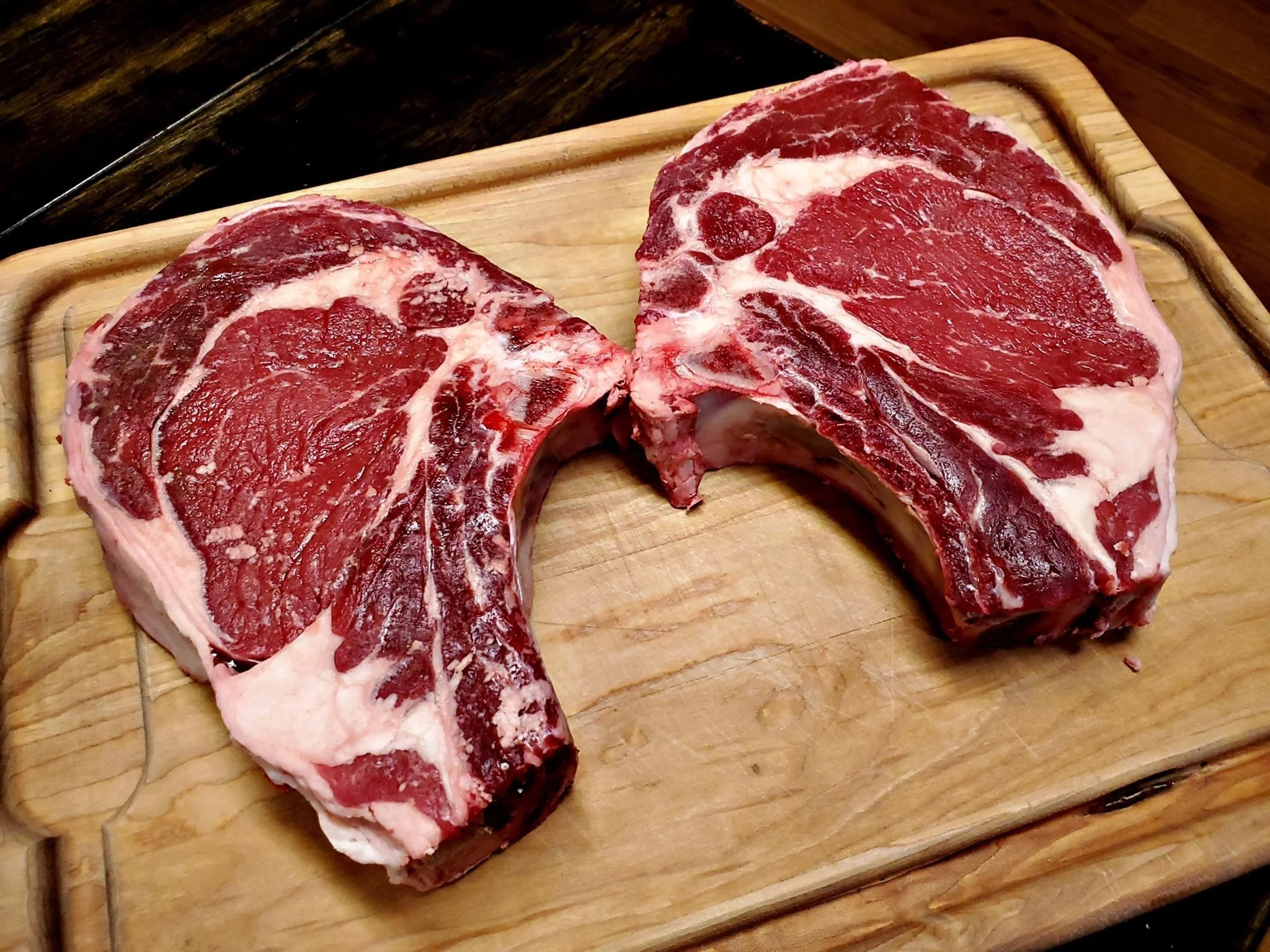 Elm Creek Beef Two raw beef steaks on a wooden cutting board.