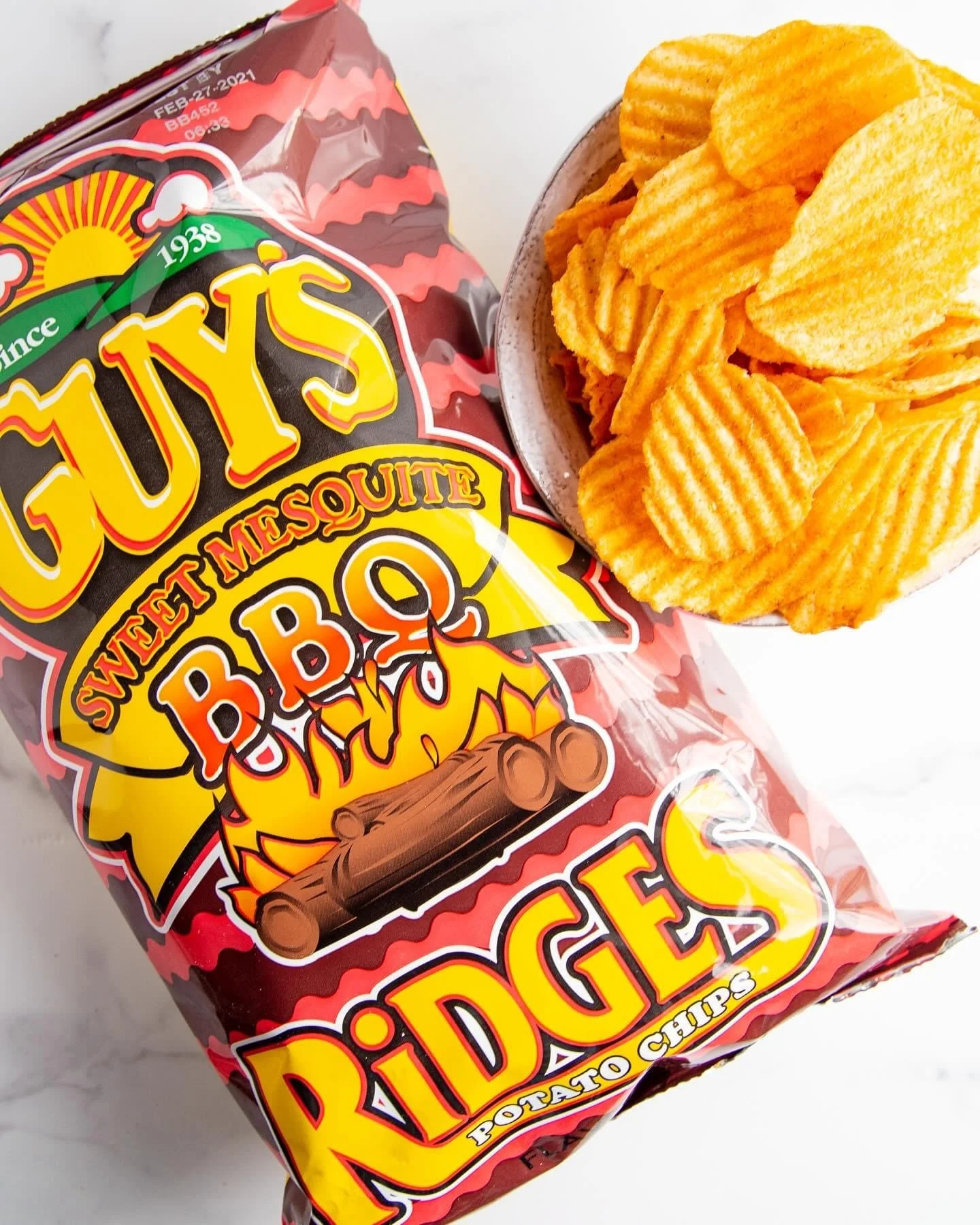 Elm Creek Beef Bag of Juicy's Sweet Mesquite BBQ Ridged Potato Chips next to a bowl of ridged potato chips.