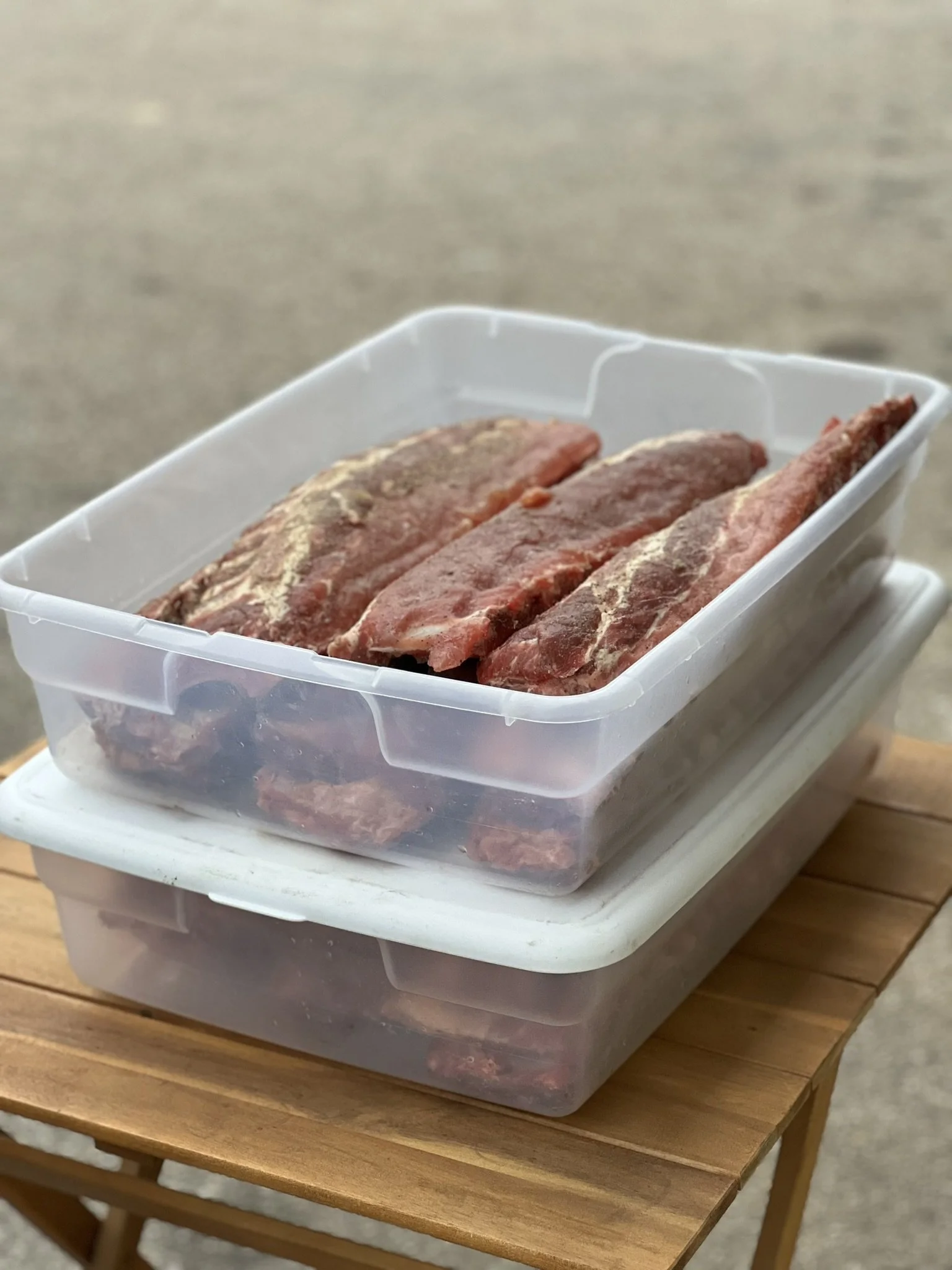Elm Creek Beef Stacked plastic containers with raw meat on a wooden table.
