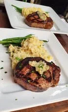 Two plated meals featuring grilled meat, mashed potatoes with gravy, green beans, and a side of lettuce.