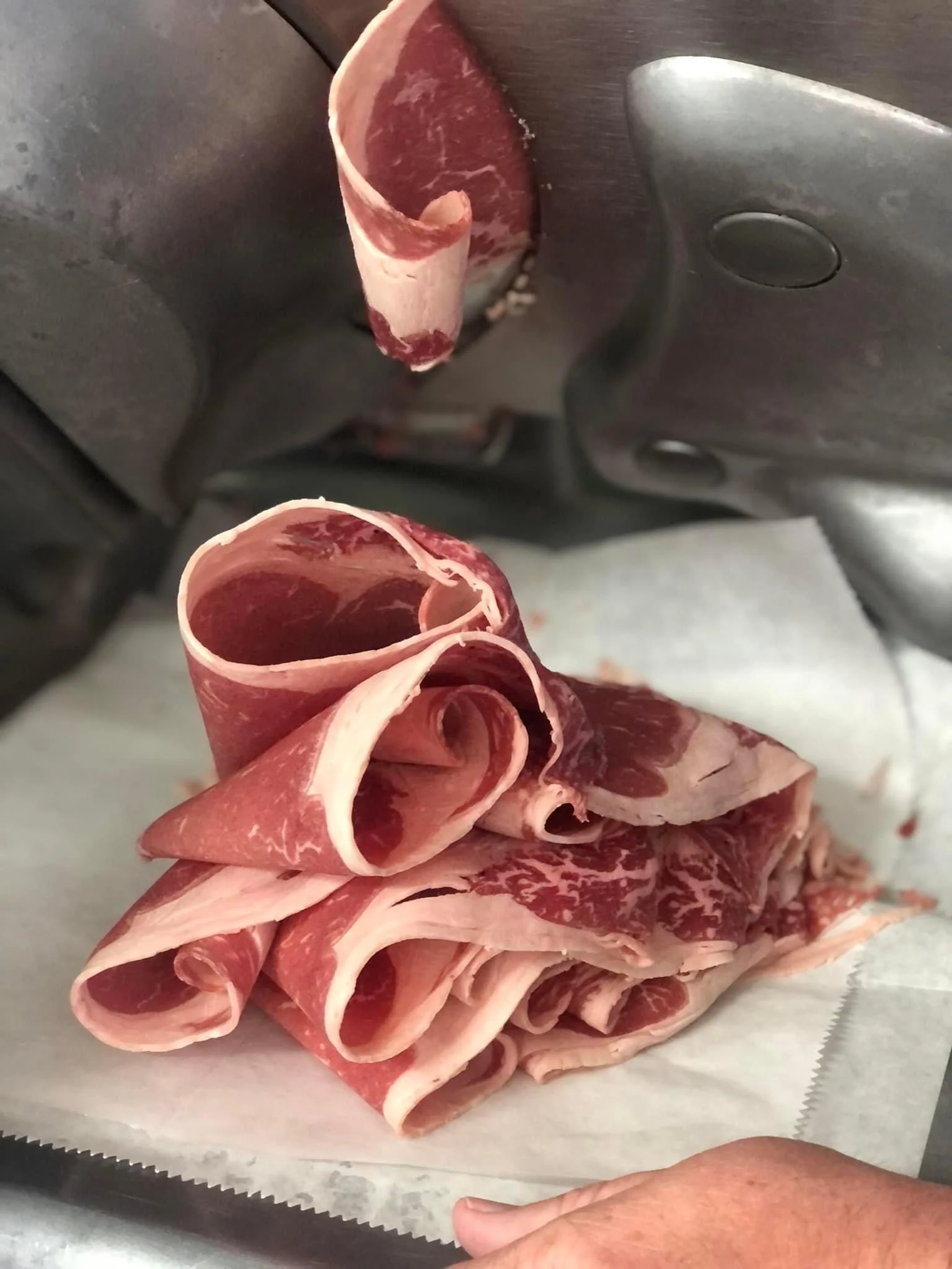 Elm Creek Beef A pile of raw, thinly sliced beef or steak with marbling on a sheet of white parchment paper.