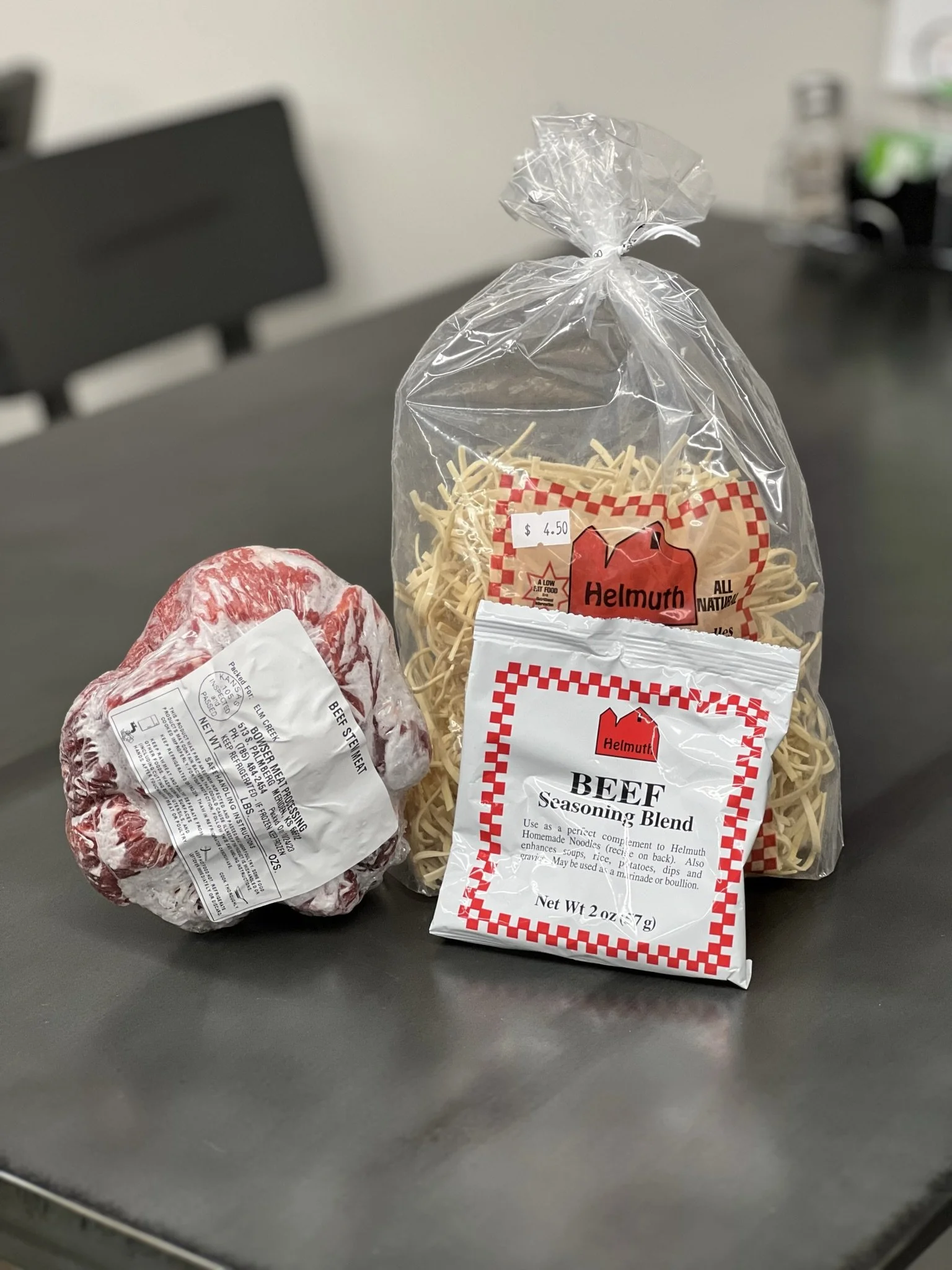 Elm Creek Beef Package of beef, a bag of beef pasta, and a piece of beef wrapped in plastic on a gray table.
