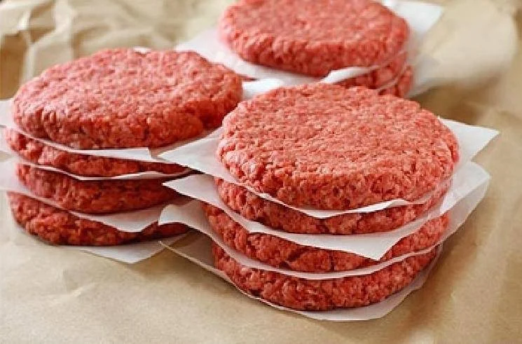 Elm Creek Beef Stacked raw beef patties separated by white paper on a paper-lined surface.