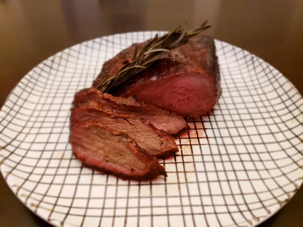 Elm Creek Beef Cooked beef steak garnished with rosemary on a patterned plate.