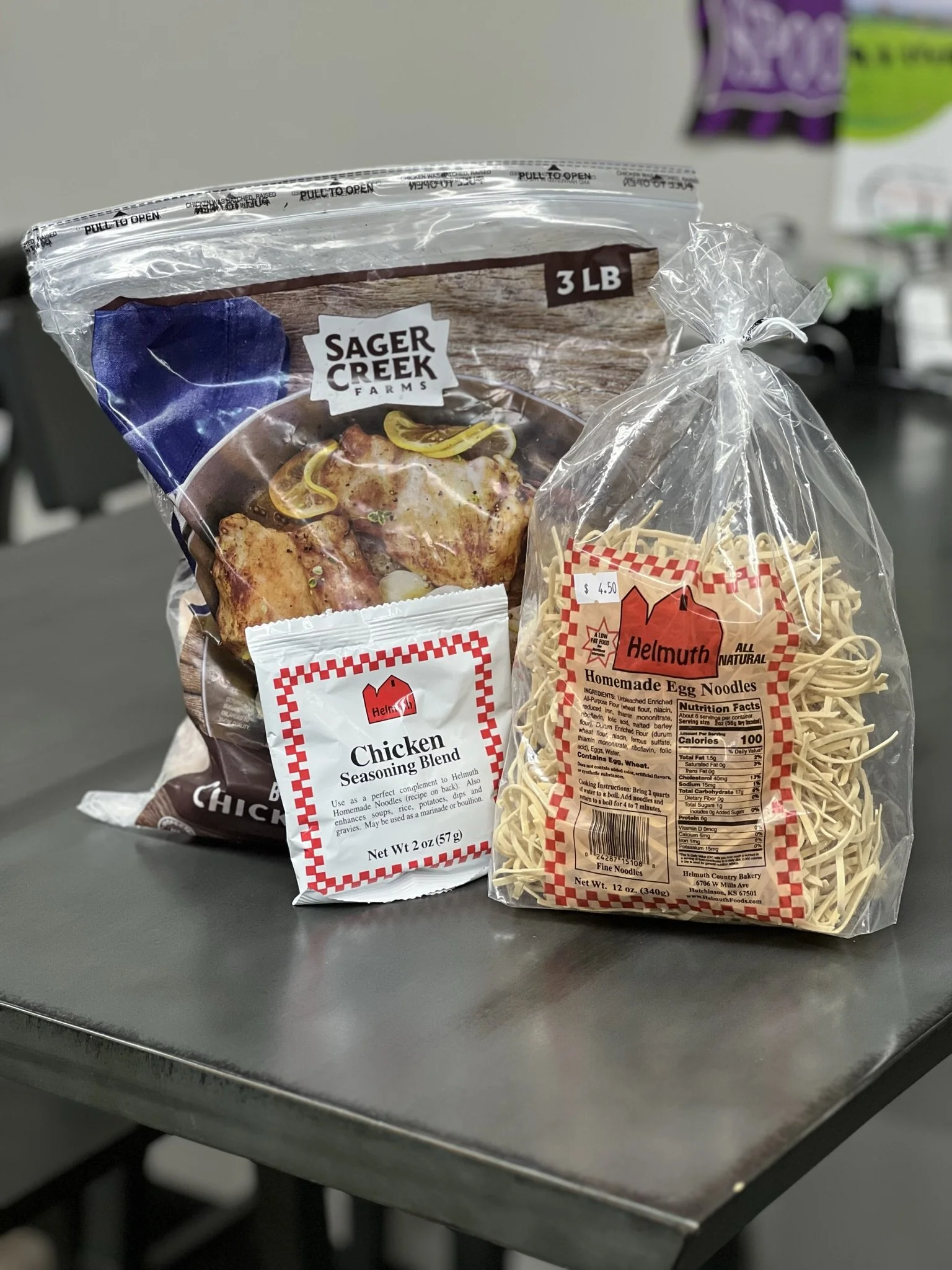 Elm Creek Beef A package of Sager Creek Farms chicken wings, a bag of Helmuth homemade egg noodles, and a packet of Helmuth chicken seasoning blend on a gray table.