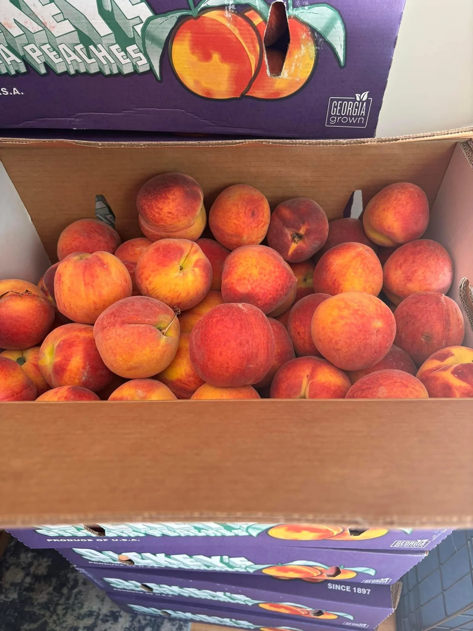 Elm Creek Beef A cardboard box filled with peaches stacked inside, with purple peach crates stacked above.