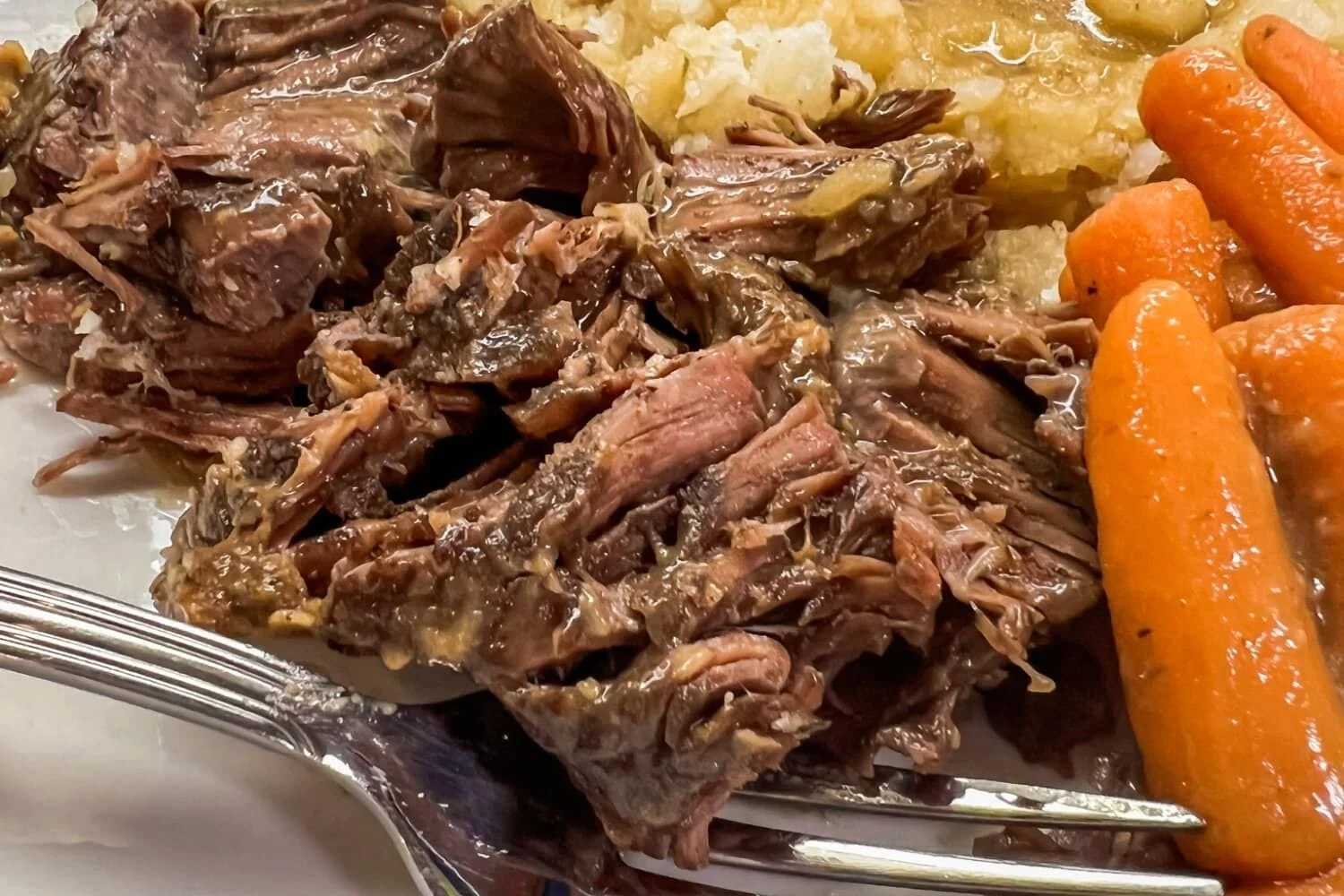 Elm Creek Beef Close-up of a plate with shredded cooked meat, mashed potatoes, and cooked carrots.