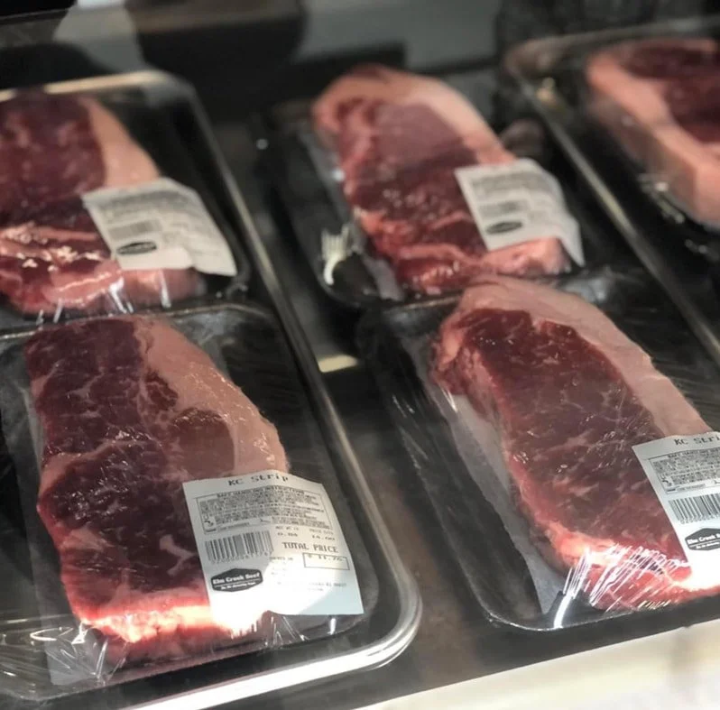 Several packages of raw beef steaks wrapped in plastic on black trays.