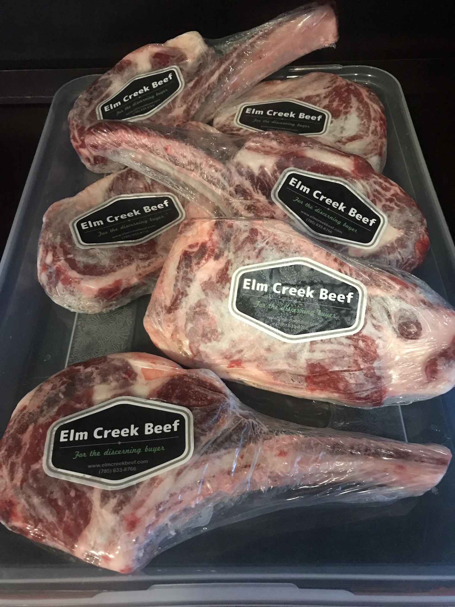 Elm Creek Beef Several packaged beef cuts labeled 'Elm Creek Beef' on a black tray, some with bones visible, wrapped in plastic.