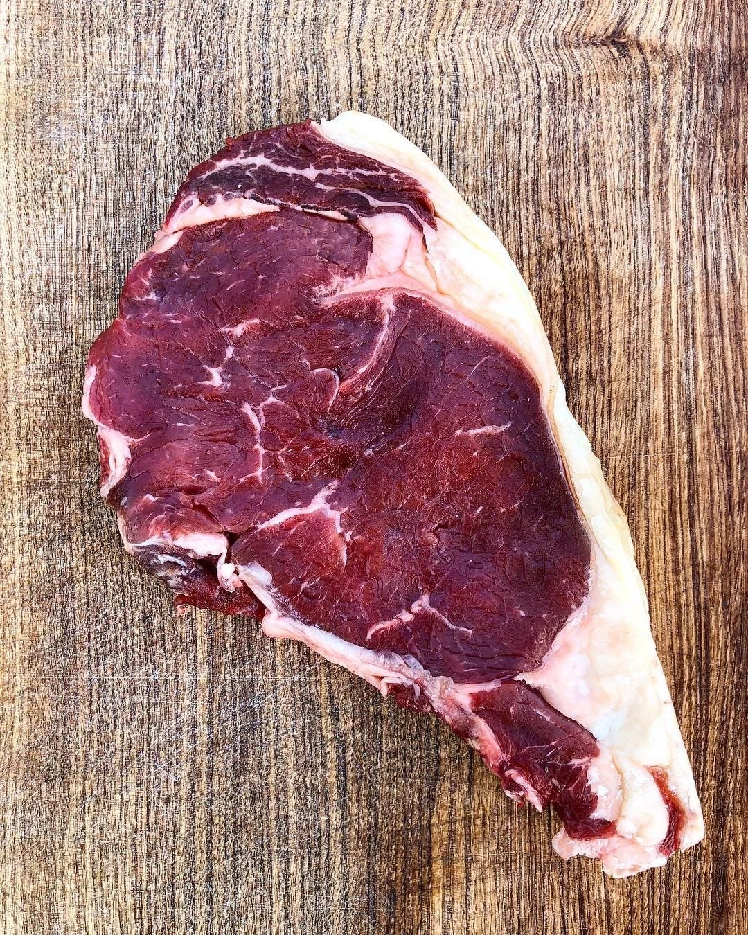 Elm Creek Beef Raw beef steak on a wooden cutting board.
