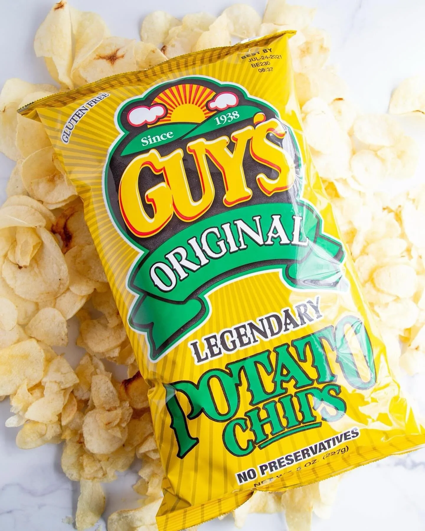 Elm Creek Beef A yellow bag of GUYS Original Legendary Potato Chips surrounded by potato chips on a white surface.