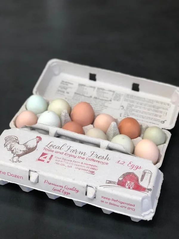 Open carton of a dozen farm fresh eggs with pastel-colored eggs labeled as local farm fresh, on a black surface.