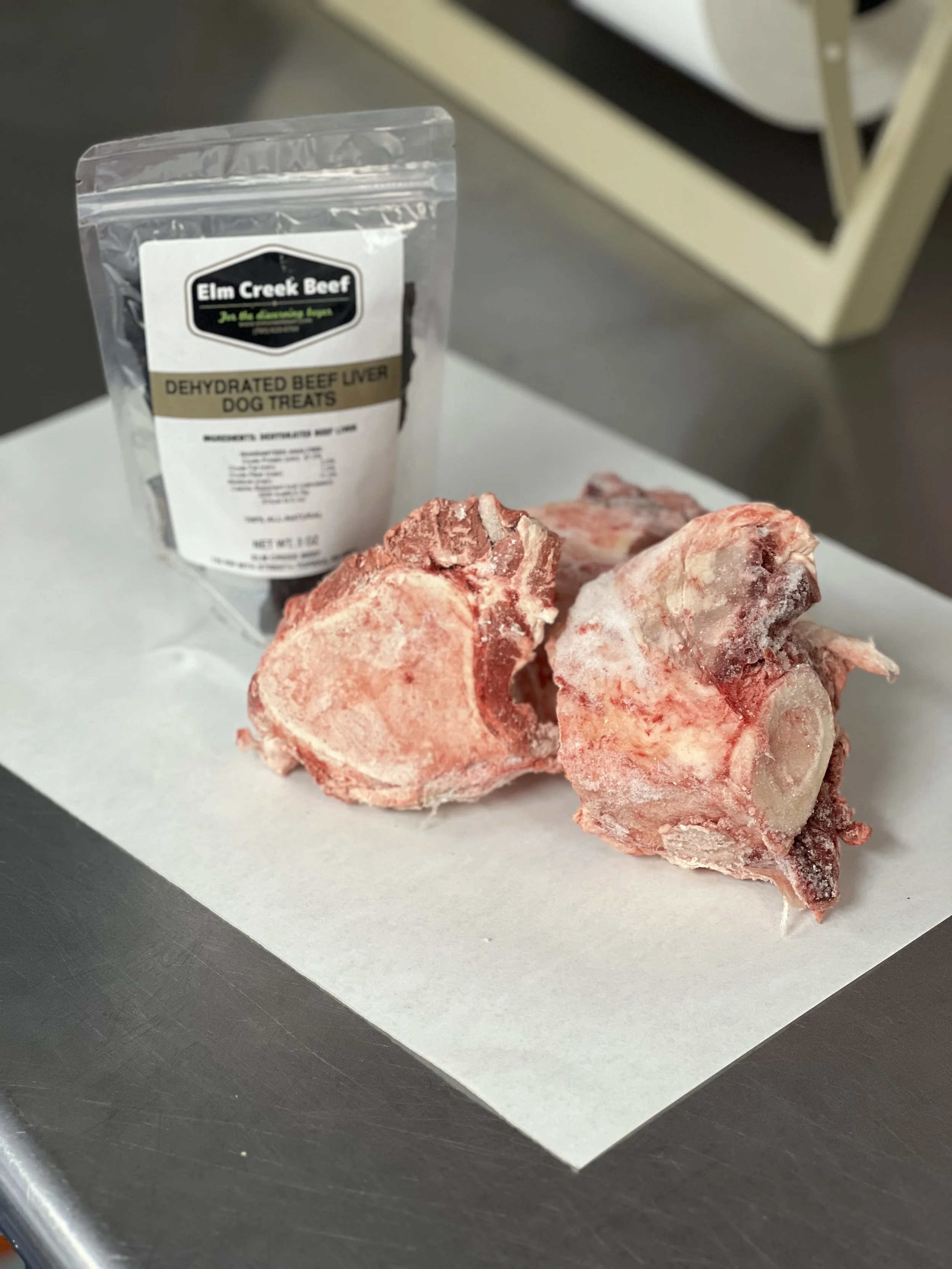Elm Creek Beef Three frozen beef bones on a white sheet of paper with a package of dehydrated beef liver dog treats nearby.