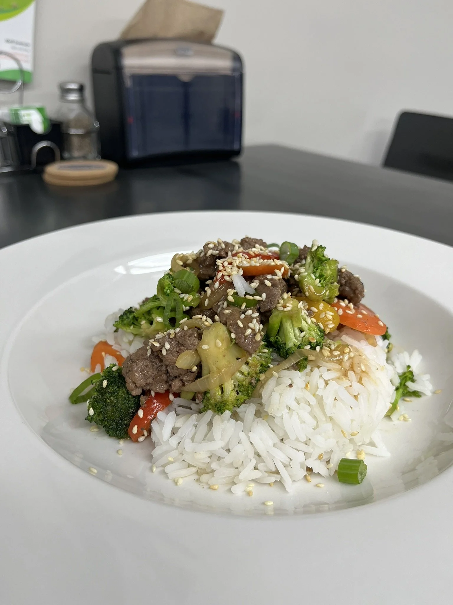 Elm Creek Beef White rice topped with stir-fried vegetables and beef, sprinkled with sesame seeds on a white plate.