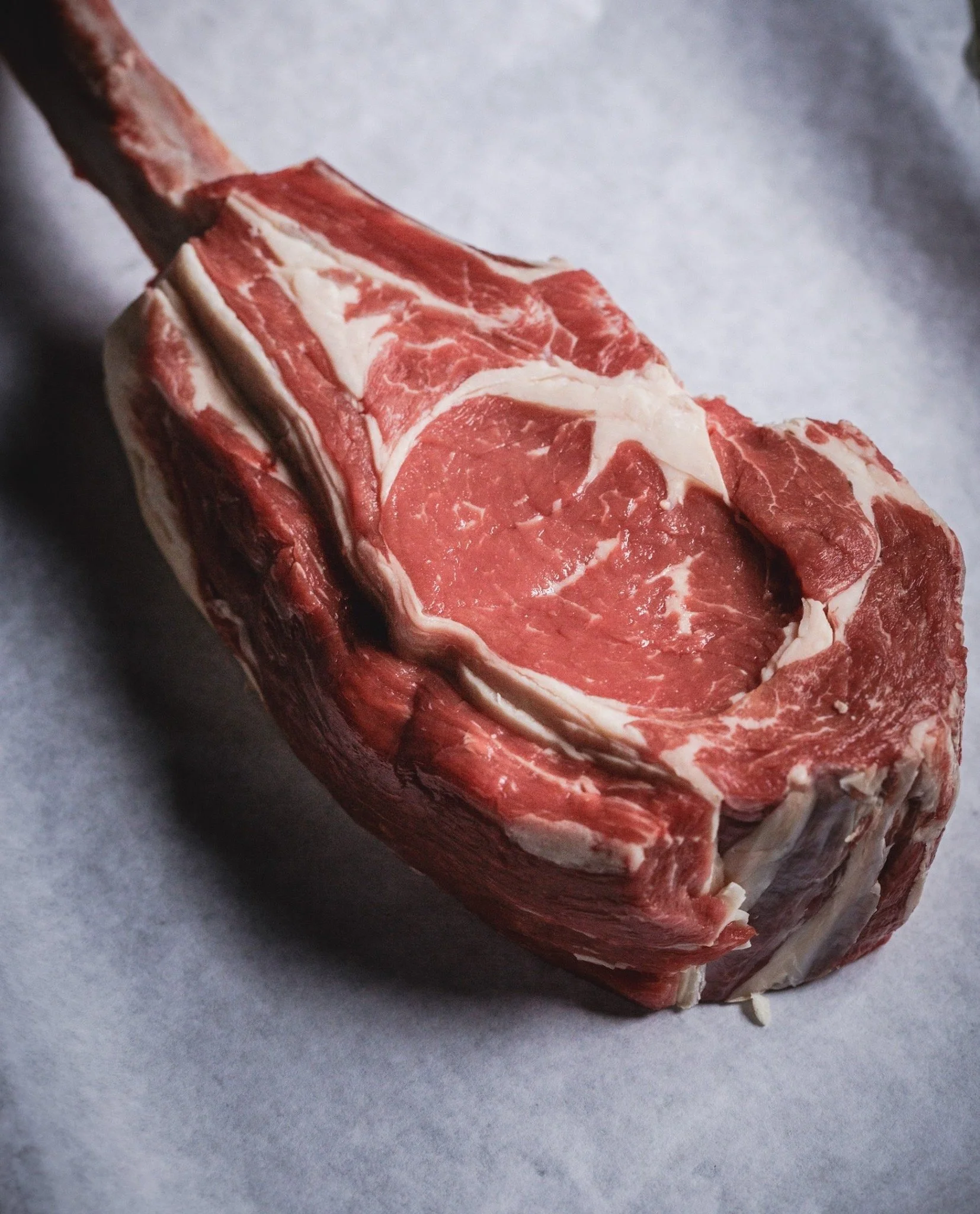 Elm Creek Beef Raw cuts of beef with marbling, showing a portion of bone, on a sheet of paper.