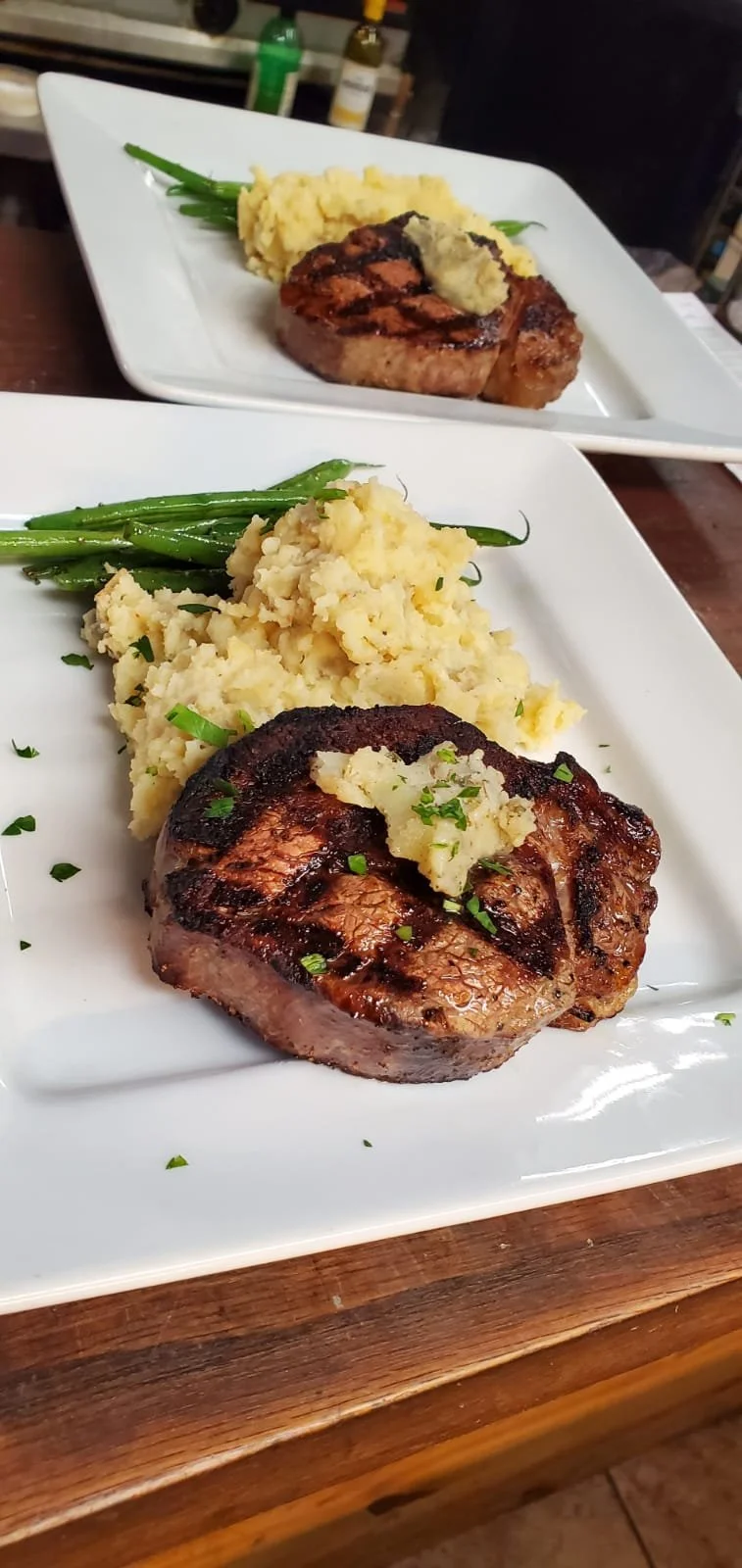 Elm Creek Beef Grilled pork chop with mashed potatoes and green beans on a white plate.
