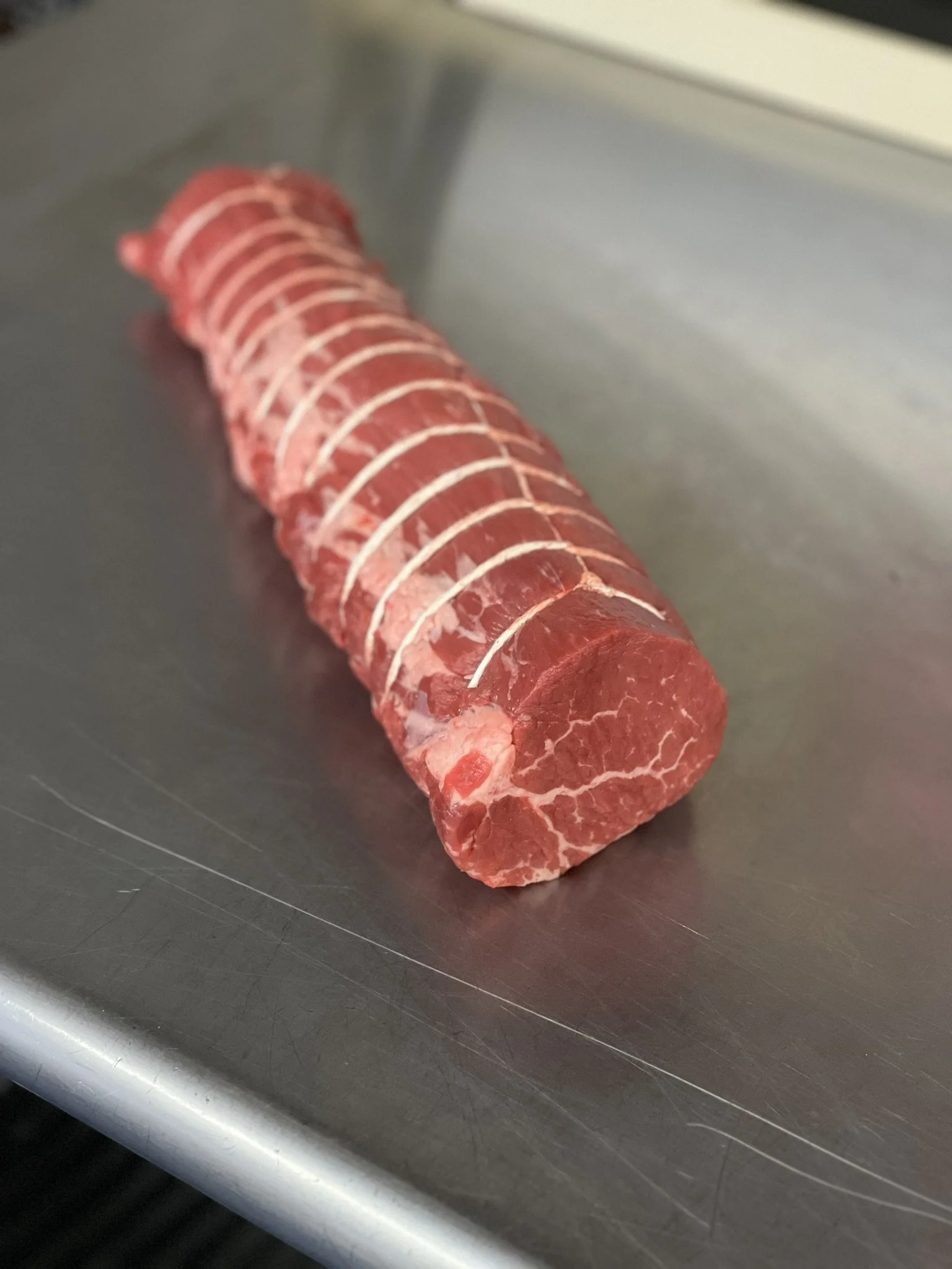 Elm Creek Beef Premium sliced raw beef tenderloin on a stainless steel surface.