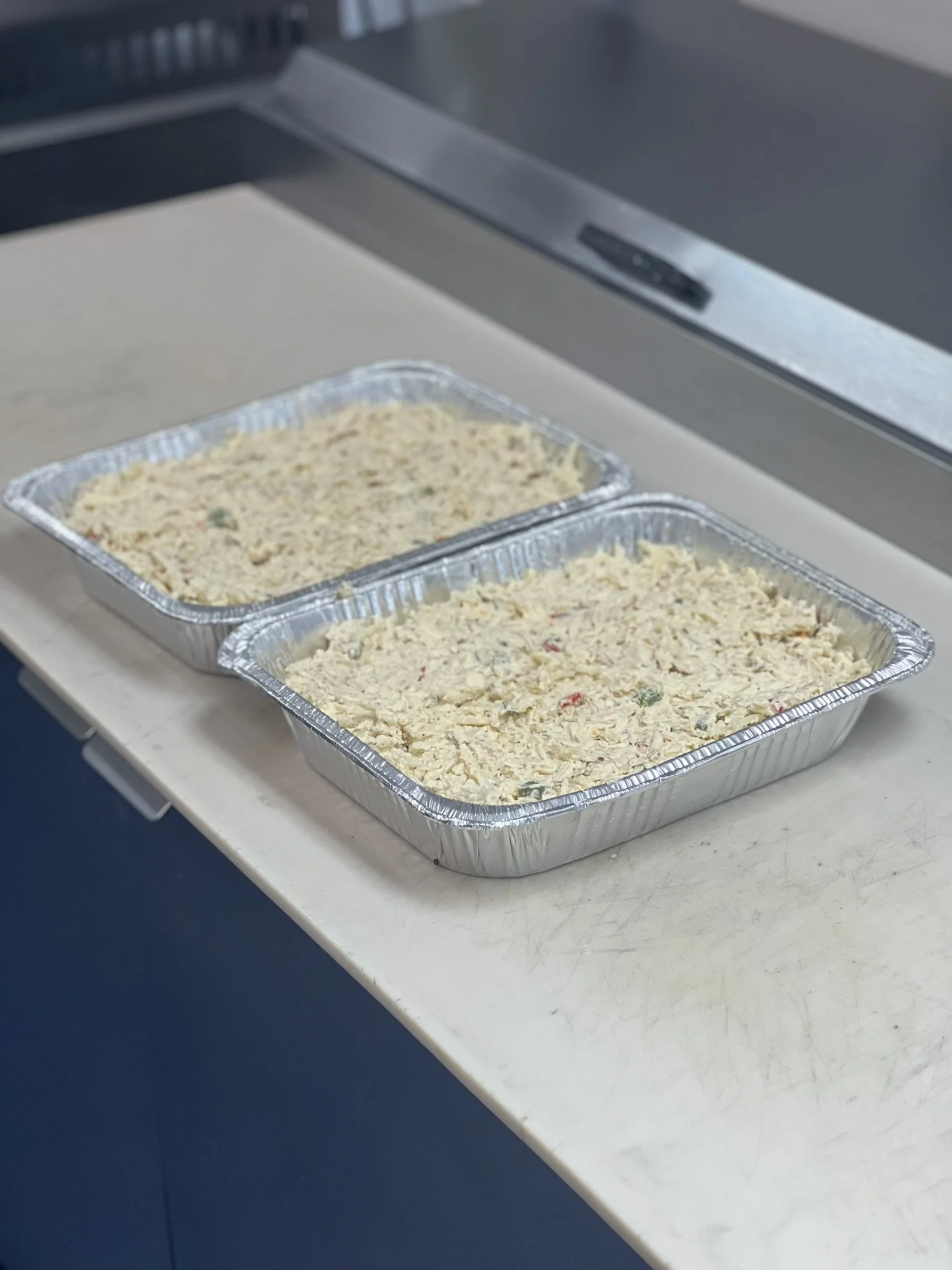 Elm Creek Beef Two aluminum foil trays filled with uncooked stuffing or bread mixture on a kitchen countertop.